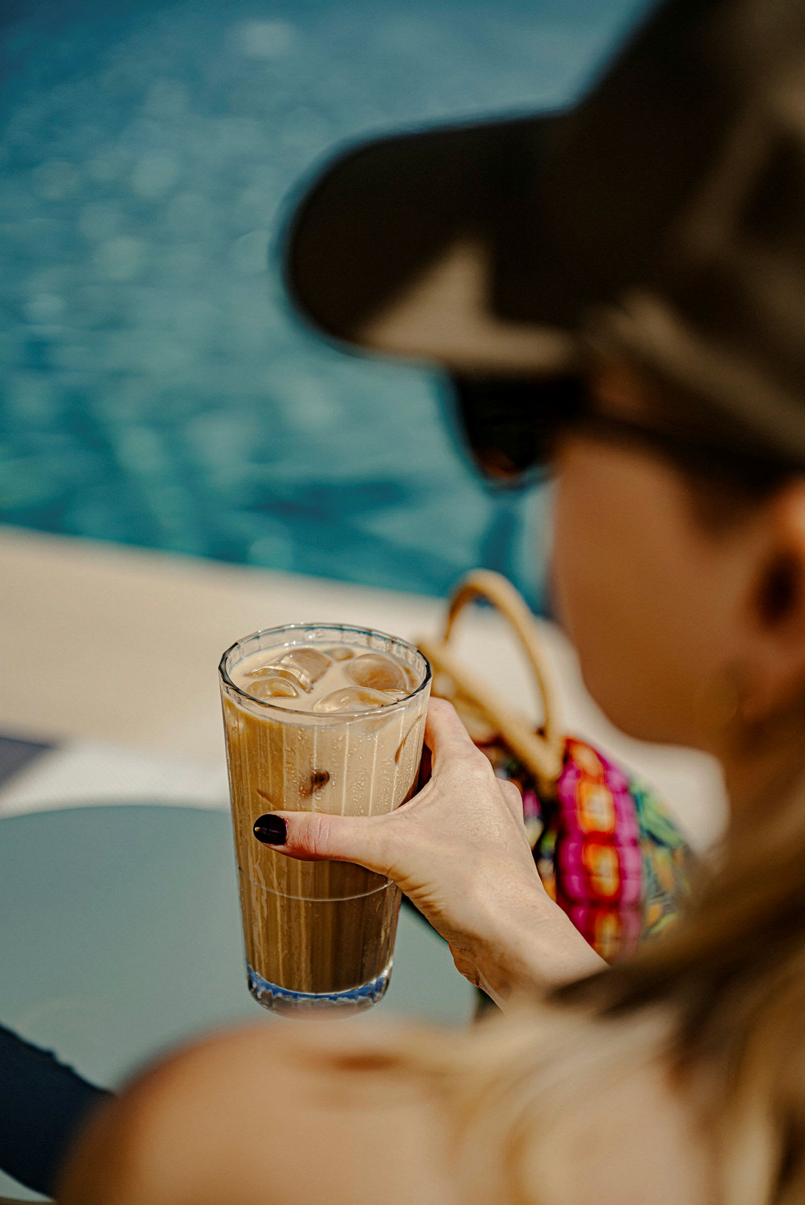 Et glass iskaffe holdes ved et svømmebasseng. (AI-generert tekst)
