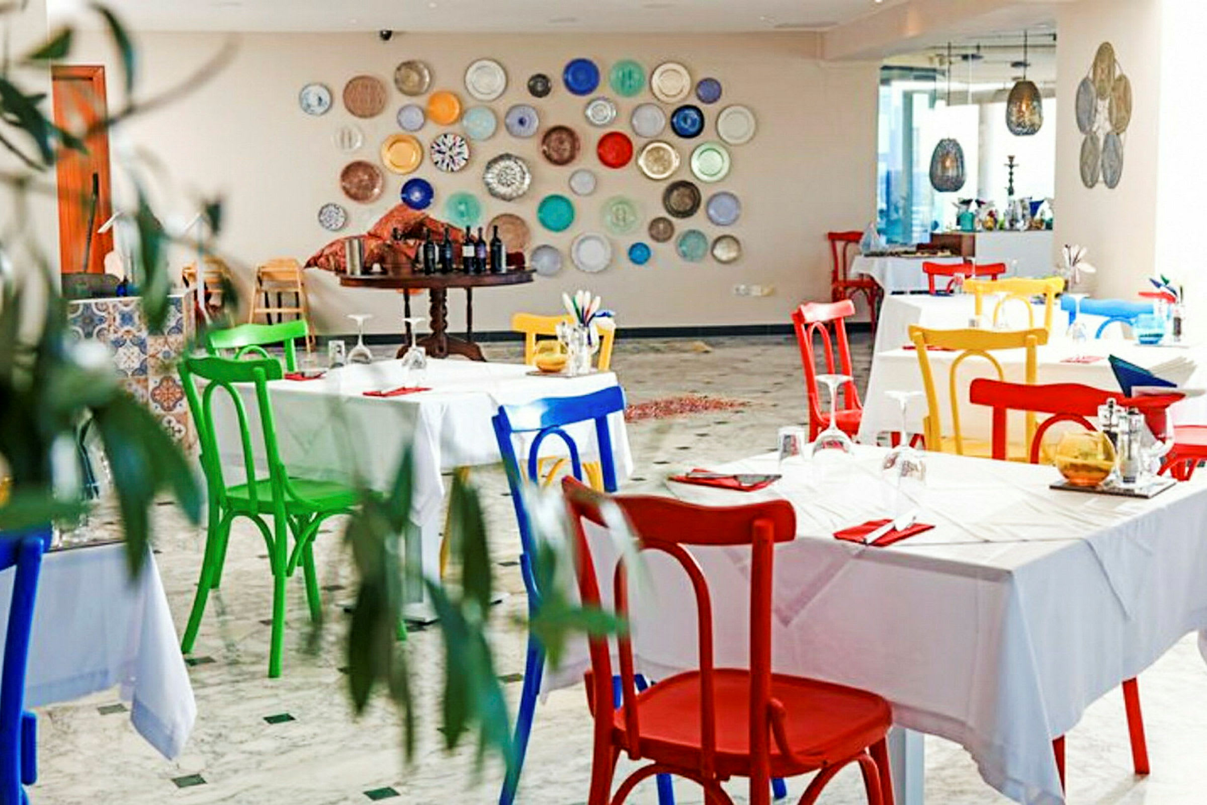 En restaurant med fargerike stoler og dekorasjonstallerkener på veggen. (AI-generert tekst)