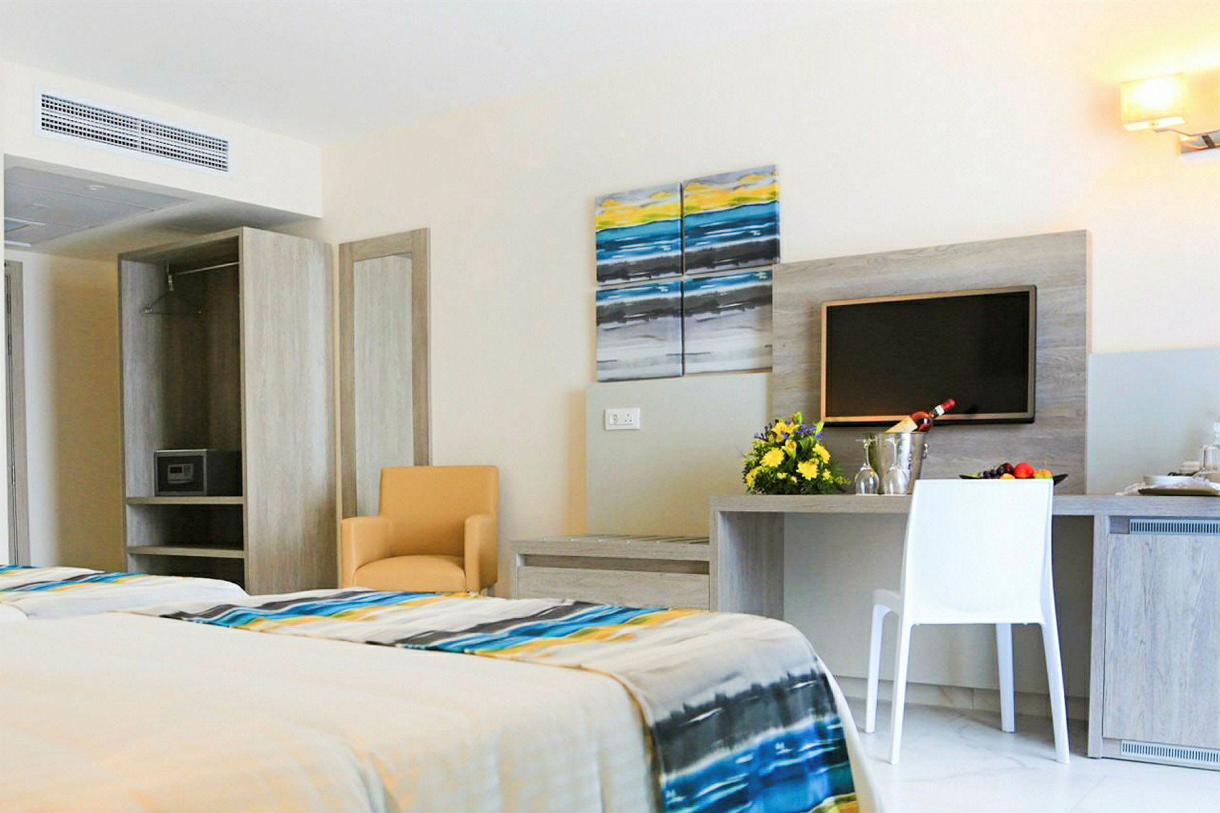 Et moderne hotellrom med en dobbeltseng, bord og stoler samt en veggmontert TV. (AI-generert tekst)