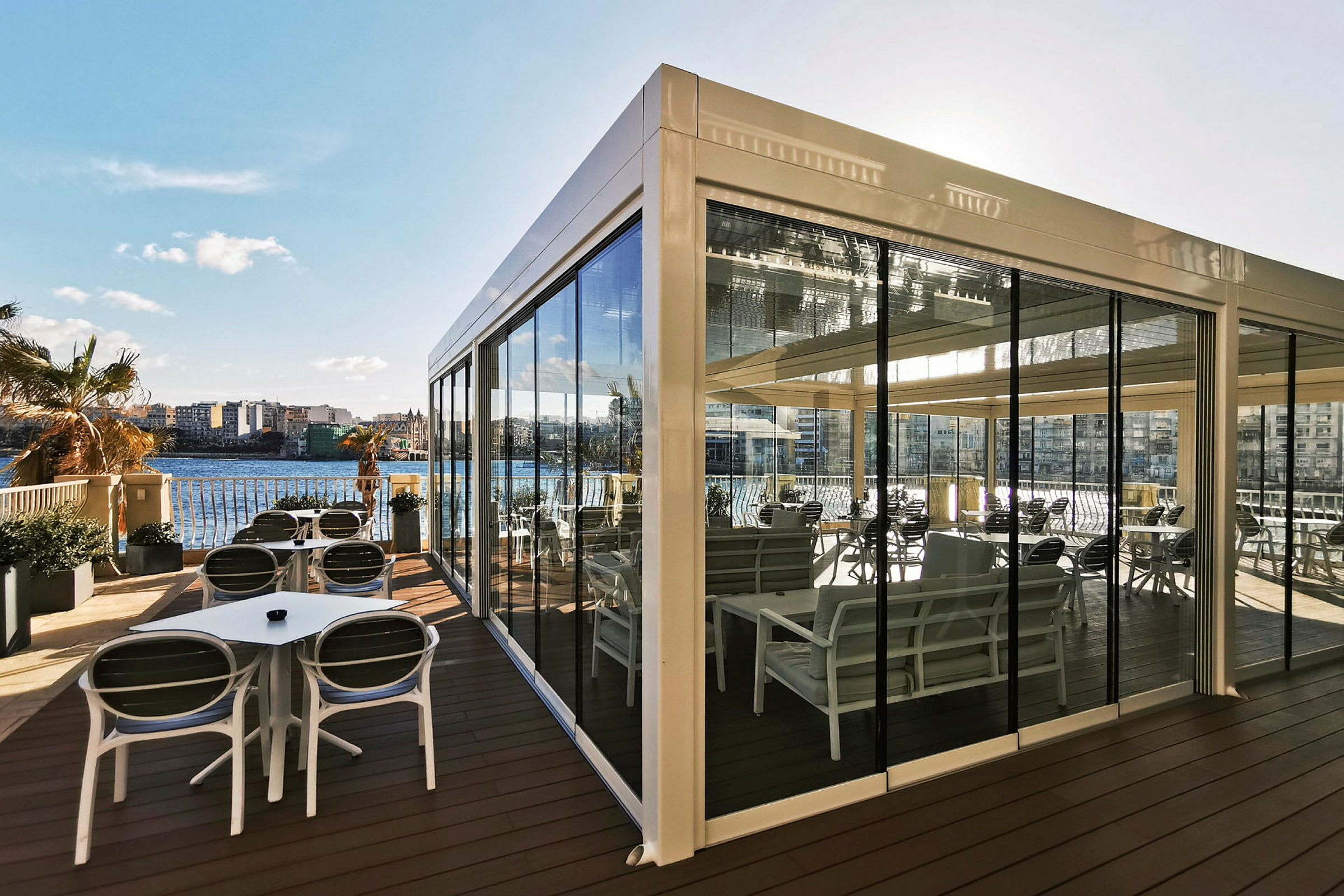 En innglasset terrasse med sittemøbler og utsikt over vannet. (AI-generert tekst)