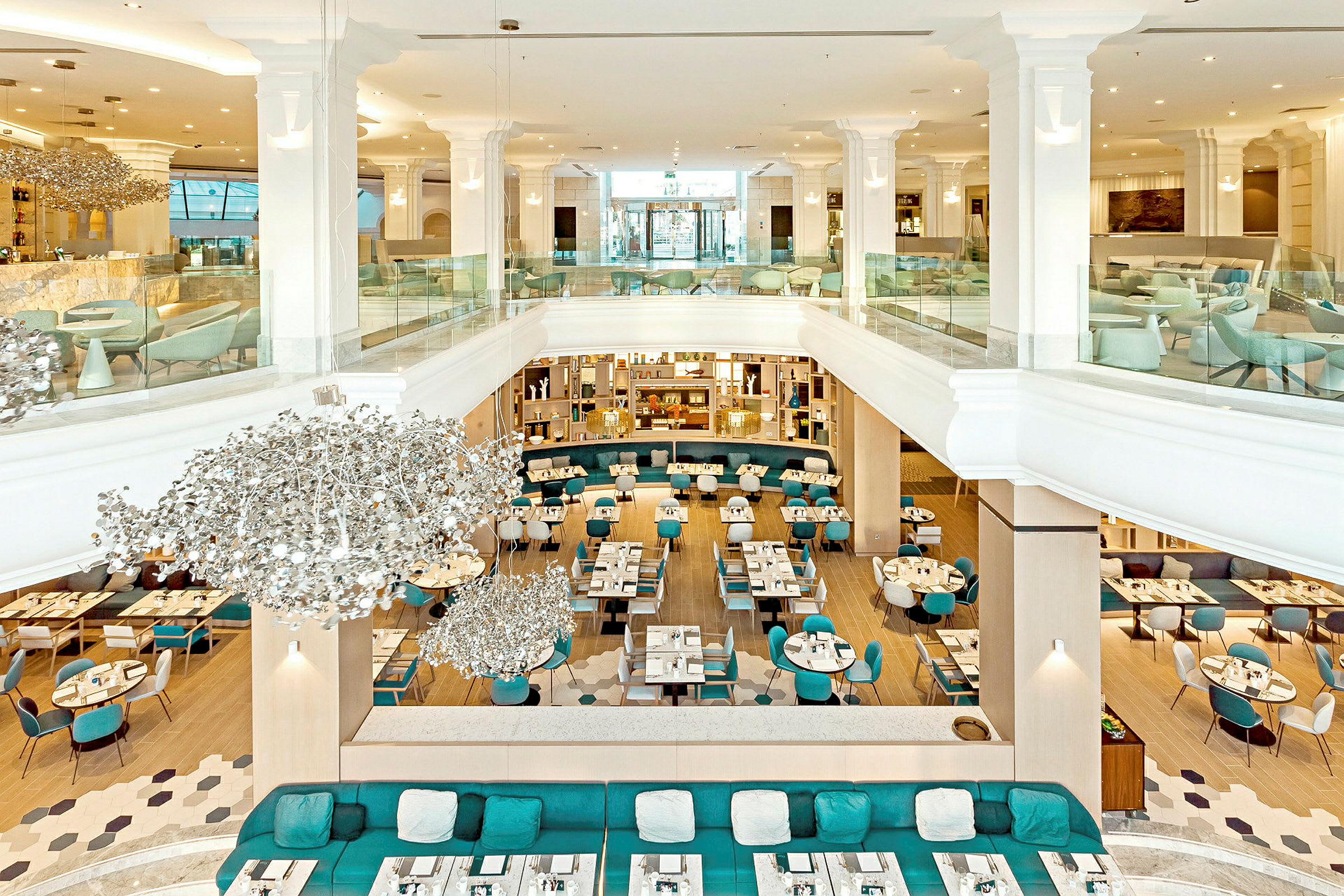 Interiør av en moderne restaurant med åpen planløsning, lyse møbler og dekorative lysekroner. (AI-generert tekst)