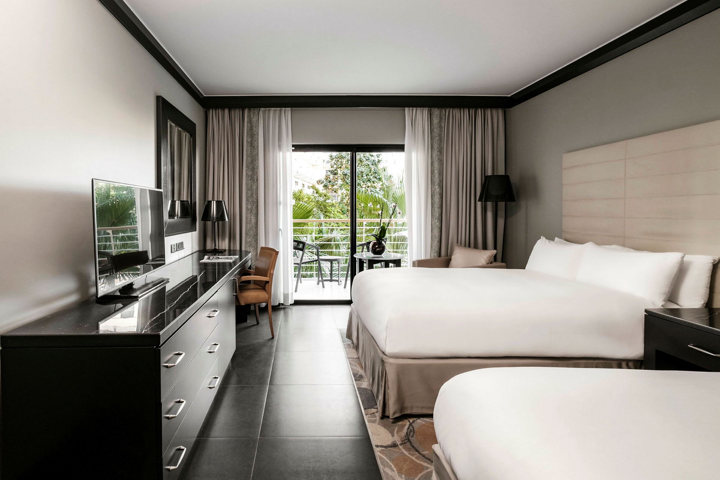 Hotellrom med to senger, skrivebord, TV og glassdør som leder ut til en balkong. (AI-generert tekst)
