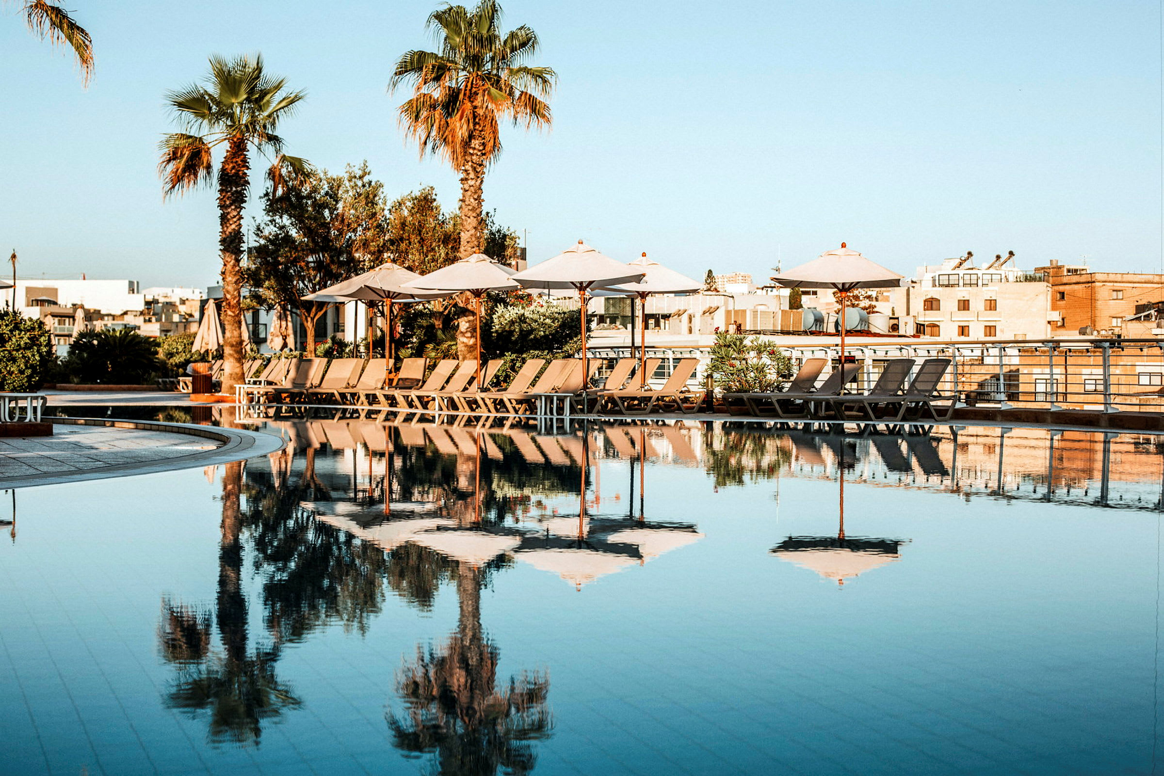 Et basseng med parasoller og solsenger på en solrik dag. (AI-generert tekst)