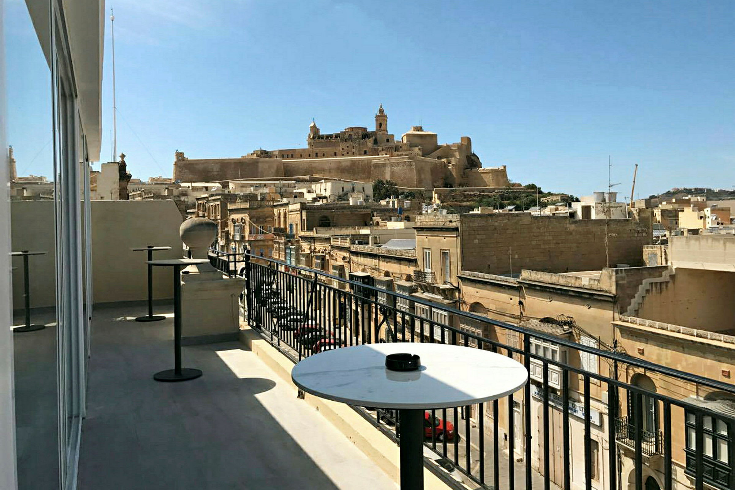 Utsikt fra en terrasse med bord over bygninger og en historisk festning på en høyde. (AI-generert tekst)