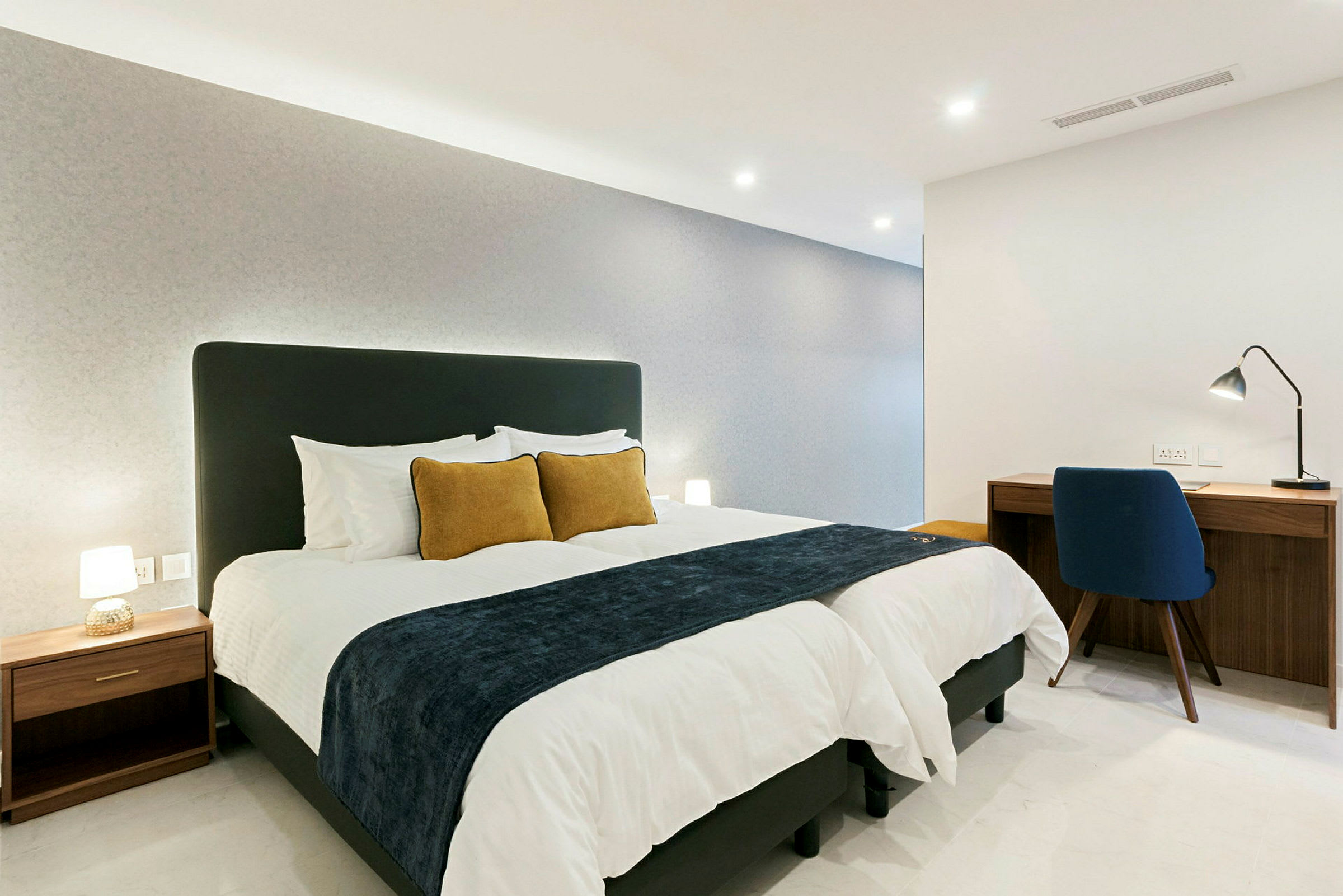 Et moderne hotellrom med en stor seng, to puter og et skrivebord med en stol. (AI-generert tekst)