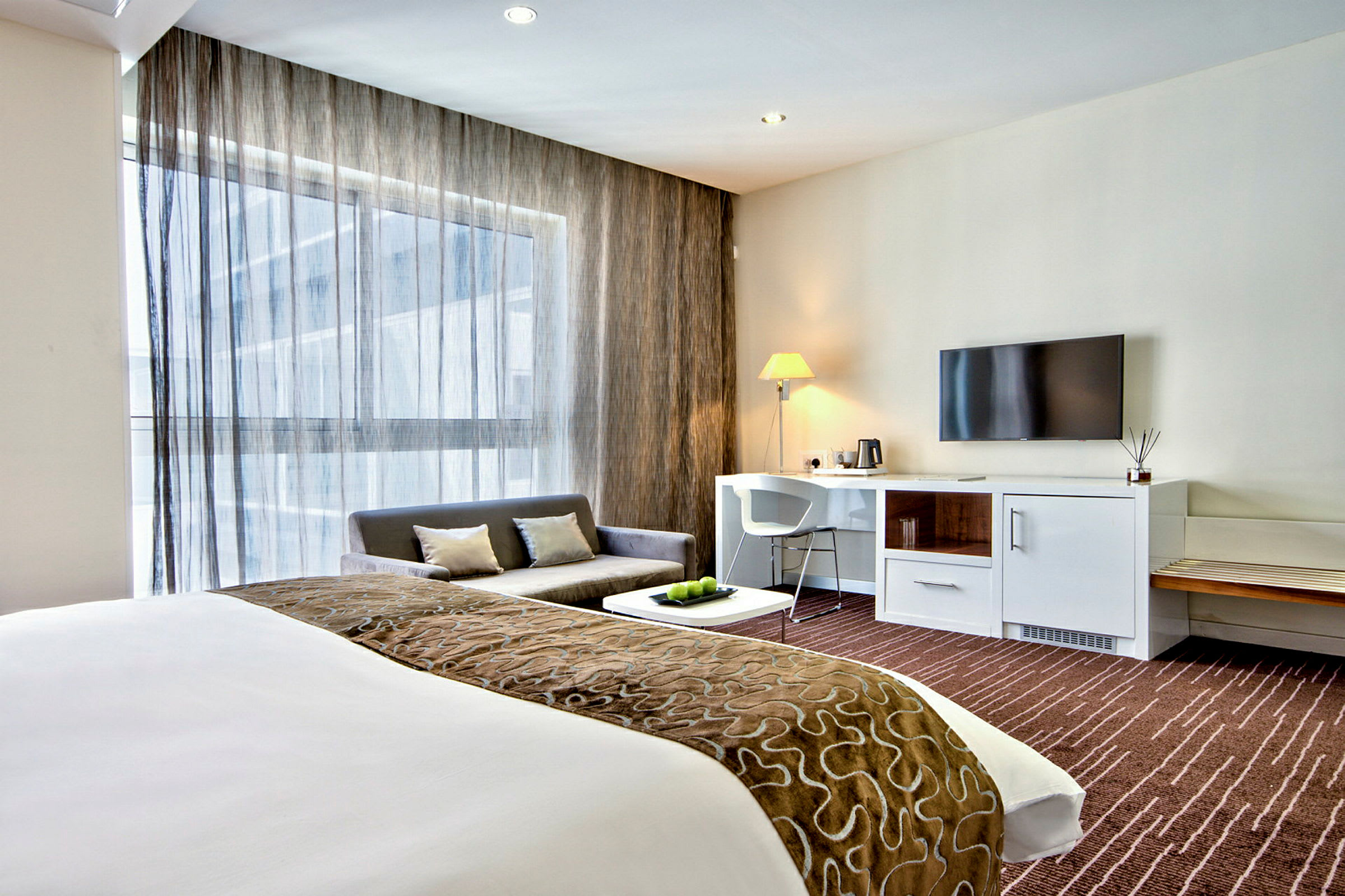 Et moderne hotellrom med seng, sofa, skrivebord og TV. (AI-generert tekst)