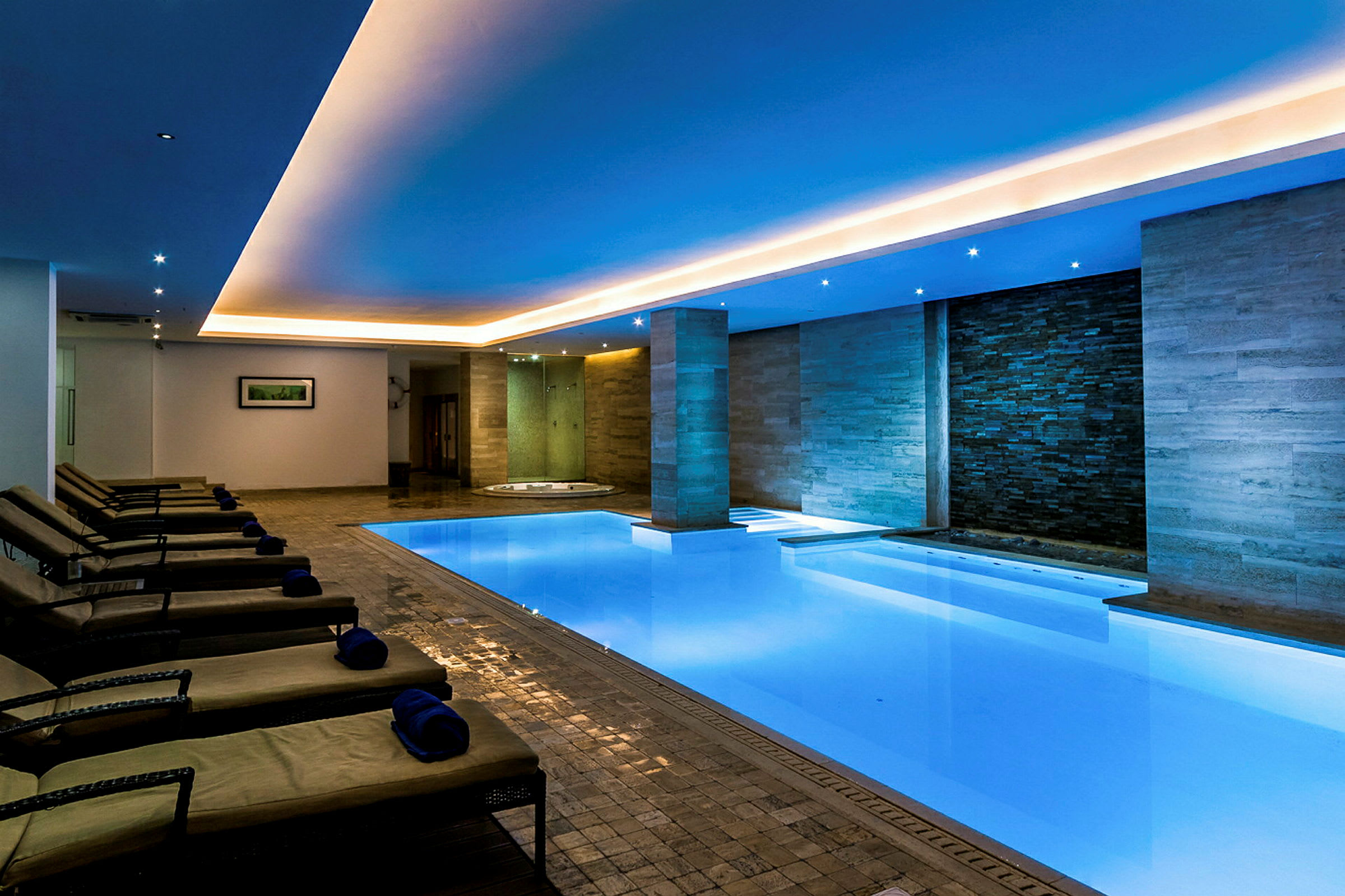 Bilde av et moderne innendørs spa med opplyst svømmebasseng, solsenger og avslappende atmosfære. (AI-generert tekst)