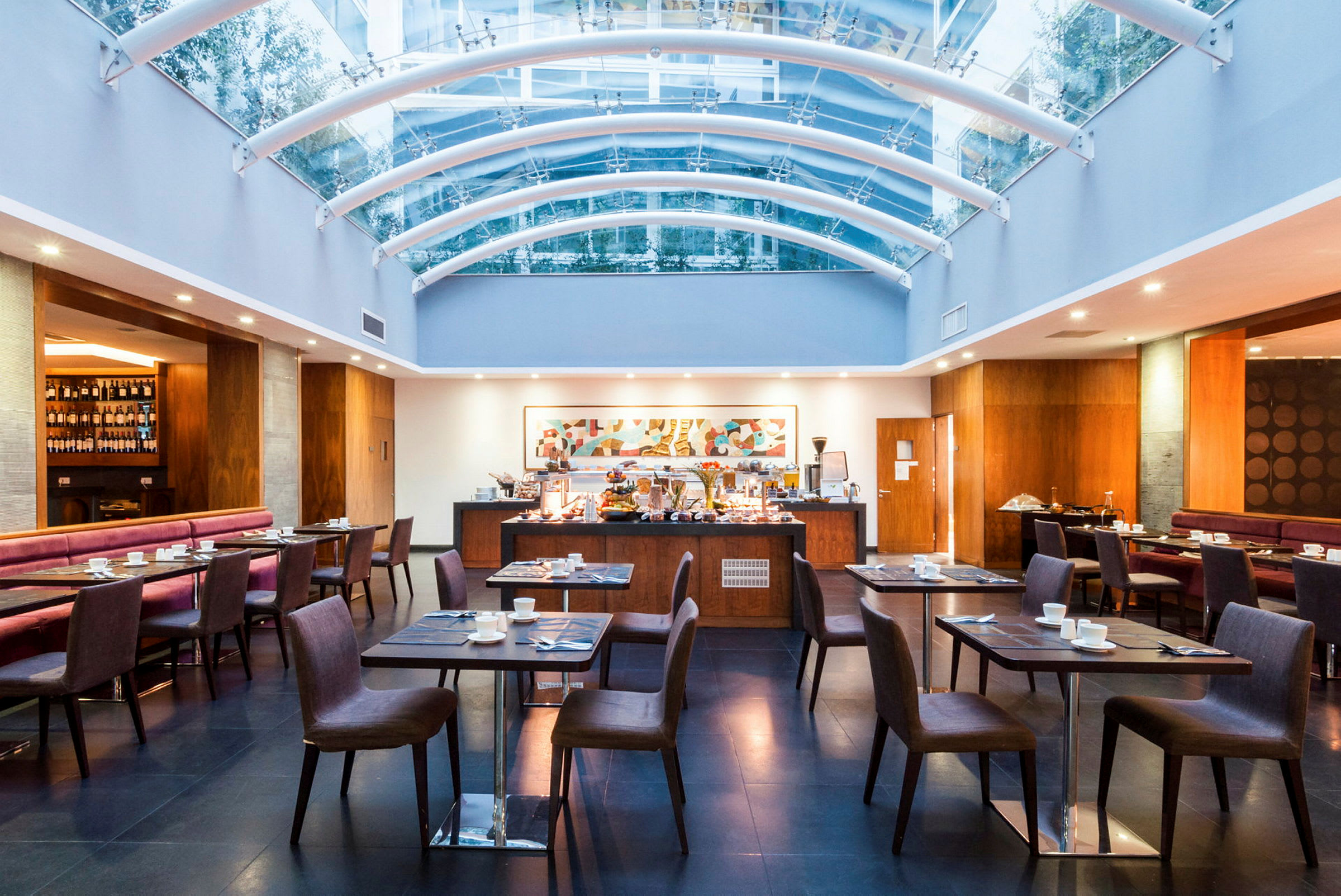 Restaurant med elegant interiør, bord og stoler, samt en gjennomsiktig takkonstruksjon. (AI-generert tekst)
