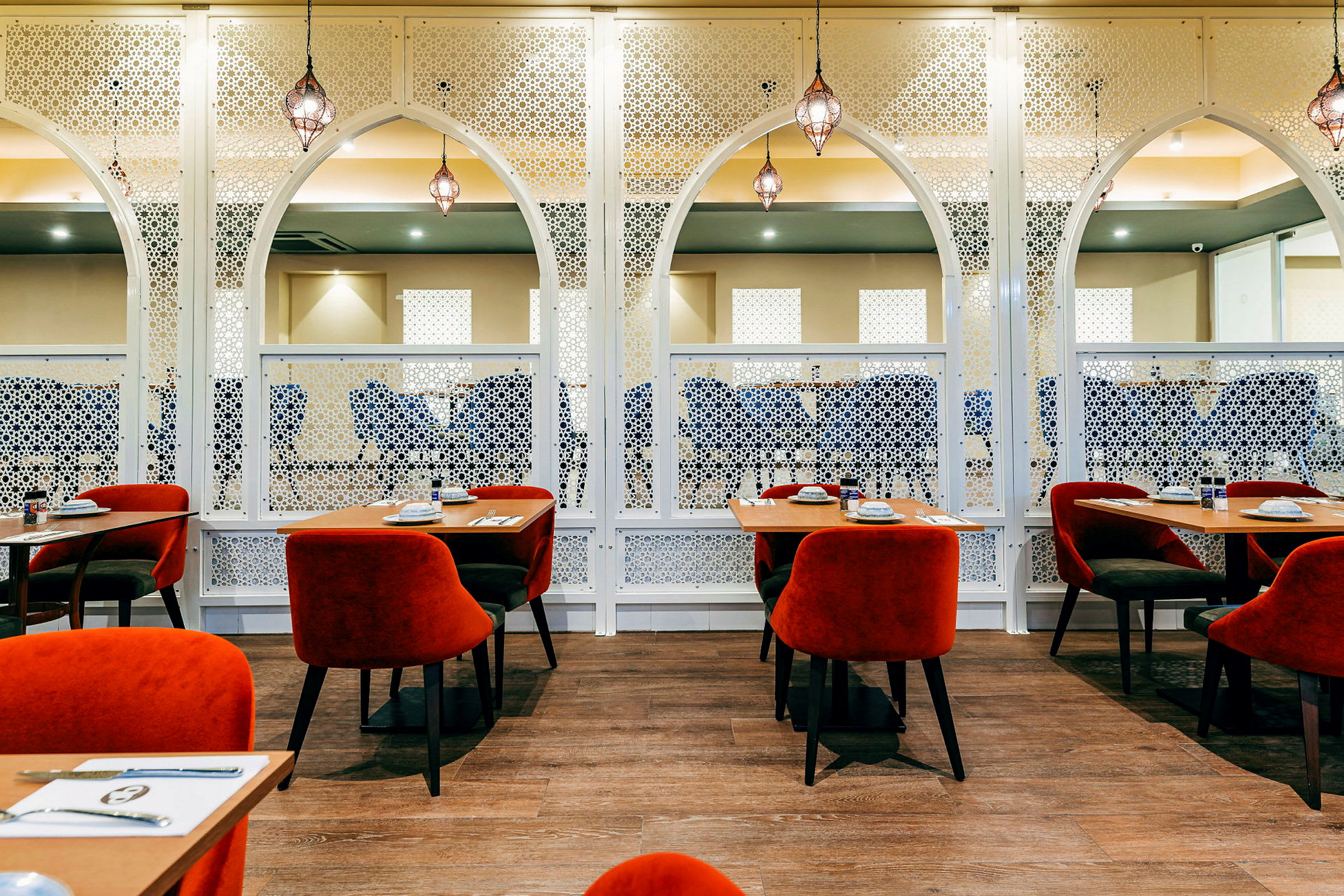 Et innredet restaurantområde med røde stoler og trebord, omgitt av hvitt dekor. (AI-generert tekst)