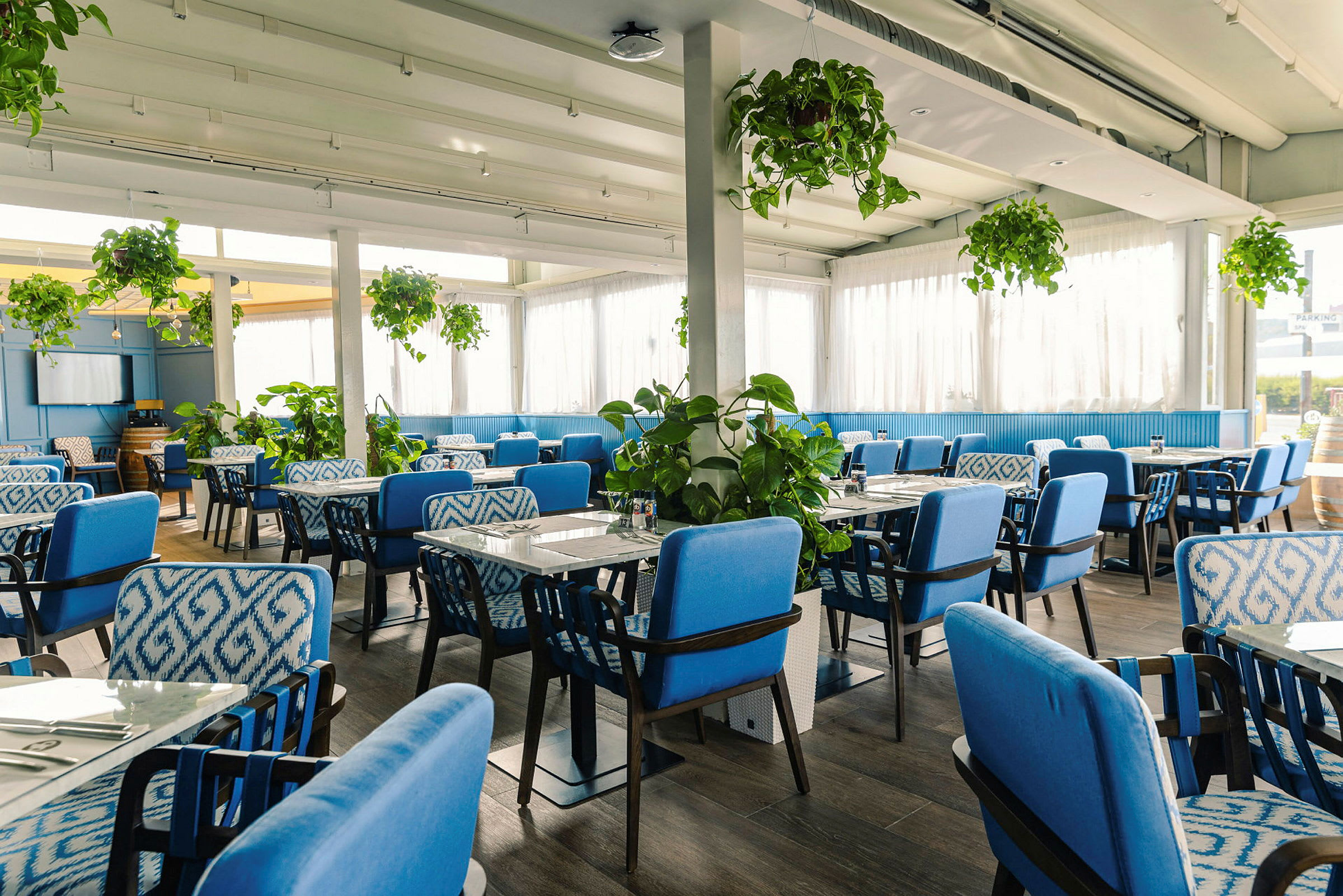 Et restaurantinteriør med blå stoler og grønne planter. (AI-generert tekst)