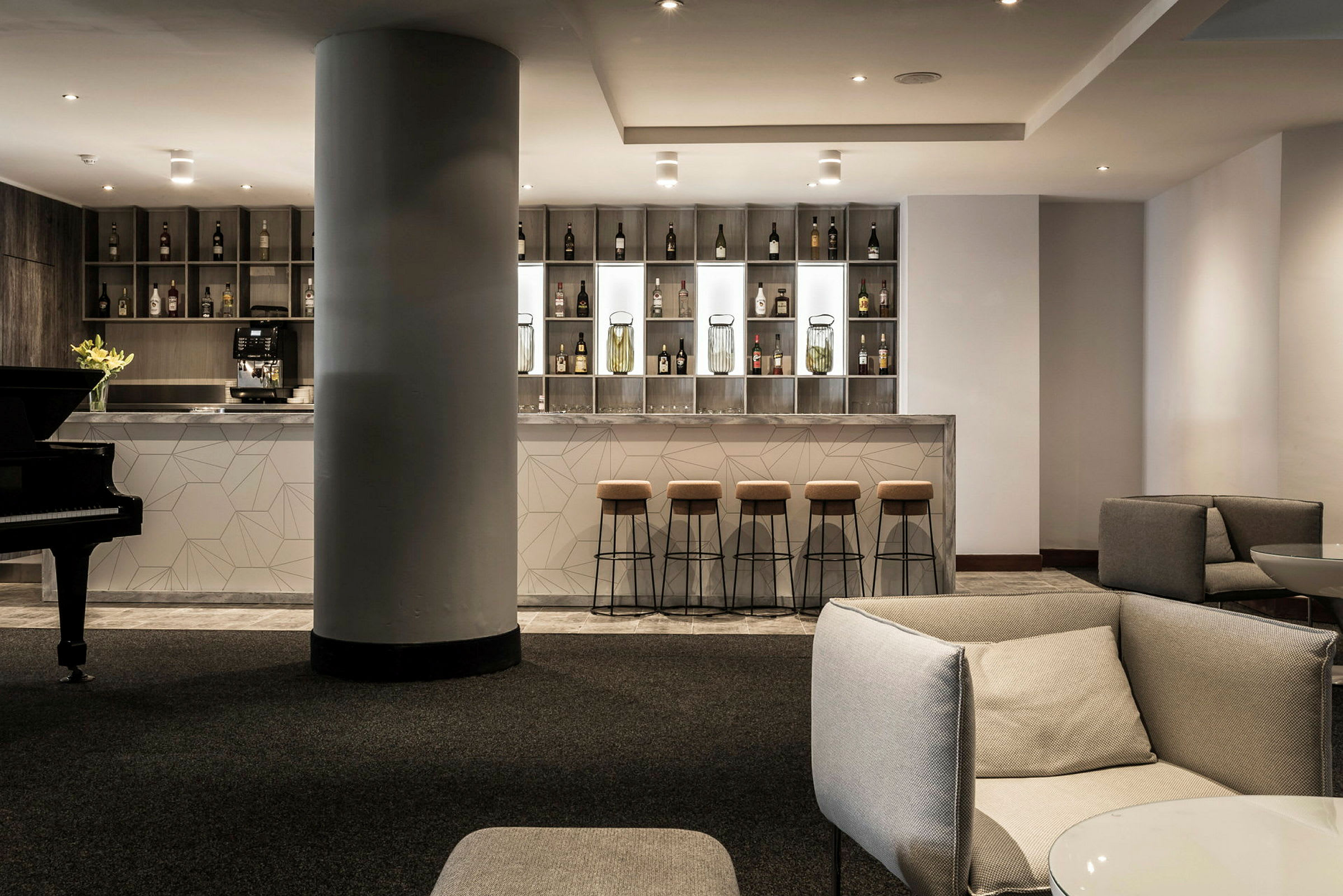 En moderne hotellbar med høye barkrakker og en stilren design. Til venstre vises et piano. (AI-generert tekst)