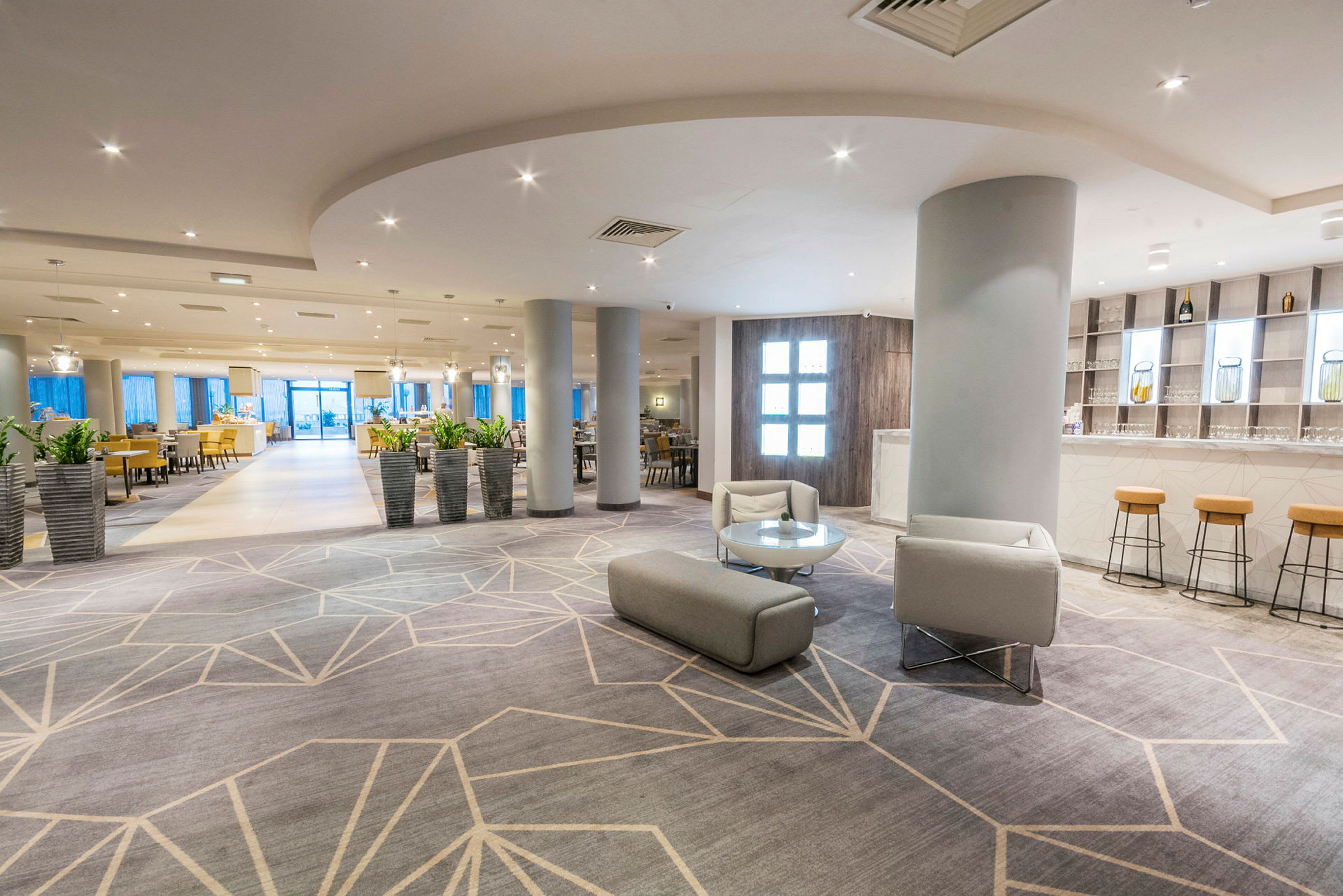 En lys og moderne hotellobby med sittemøbler og flere planter i potter. (AI-generert tekst)