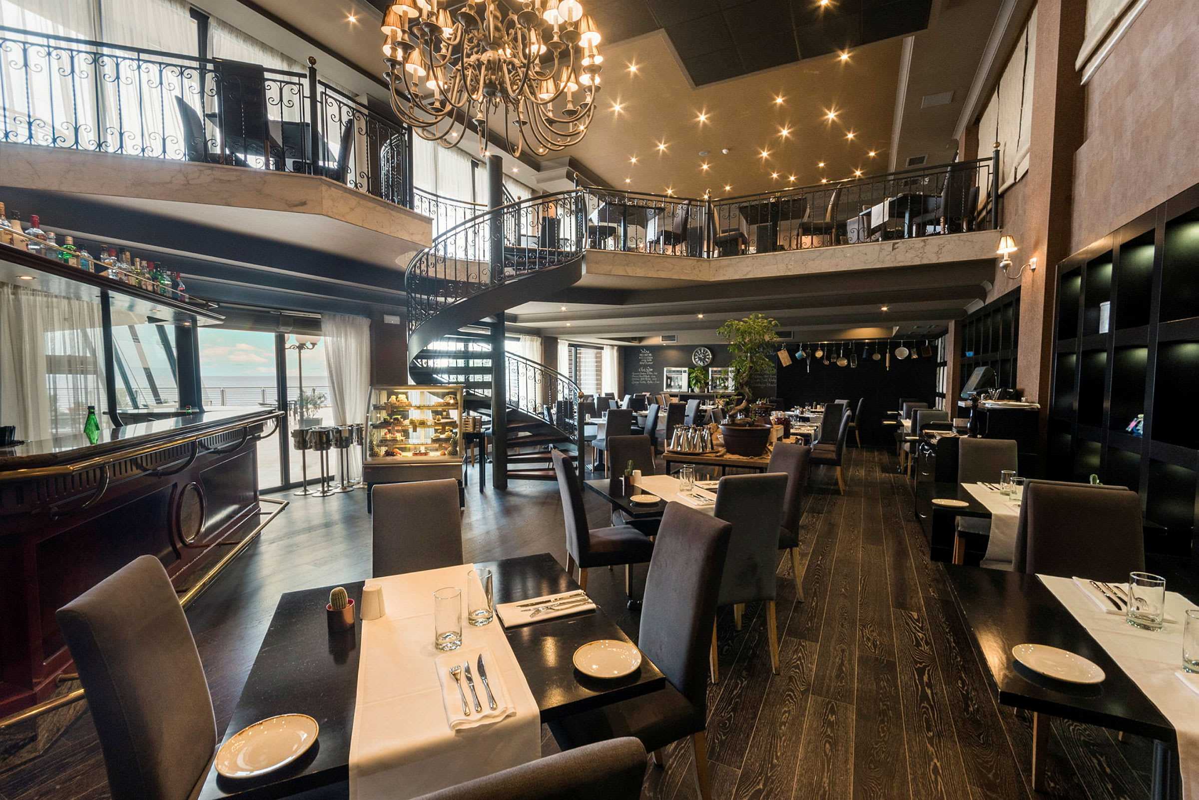 En romslig restaurant med elegante møbler og en spiraltrapp i midten. (AI-generert tekst)