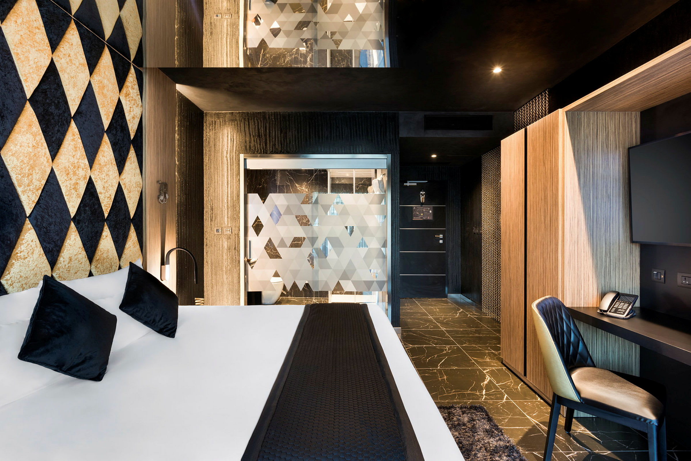 Hotellrom med moderne design, seng med hvite laken og svarte puter, samt arbeidsområde med stol, skrivebord og TV. (AI-generert tekst)