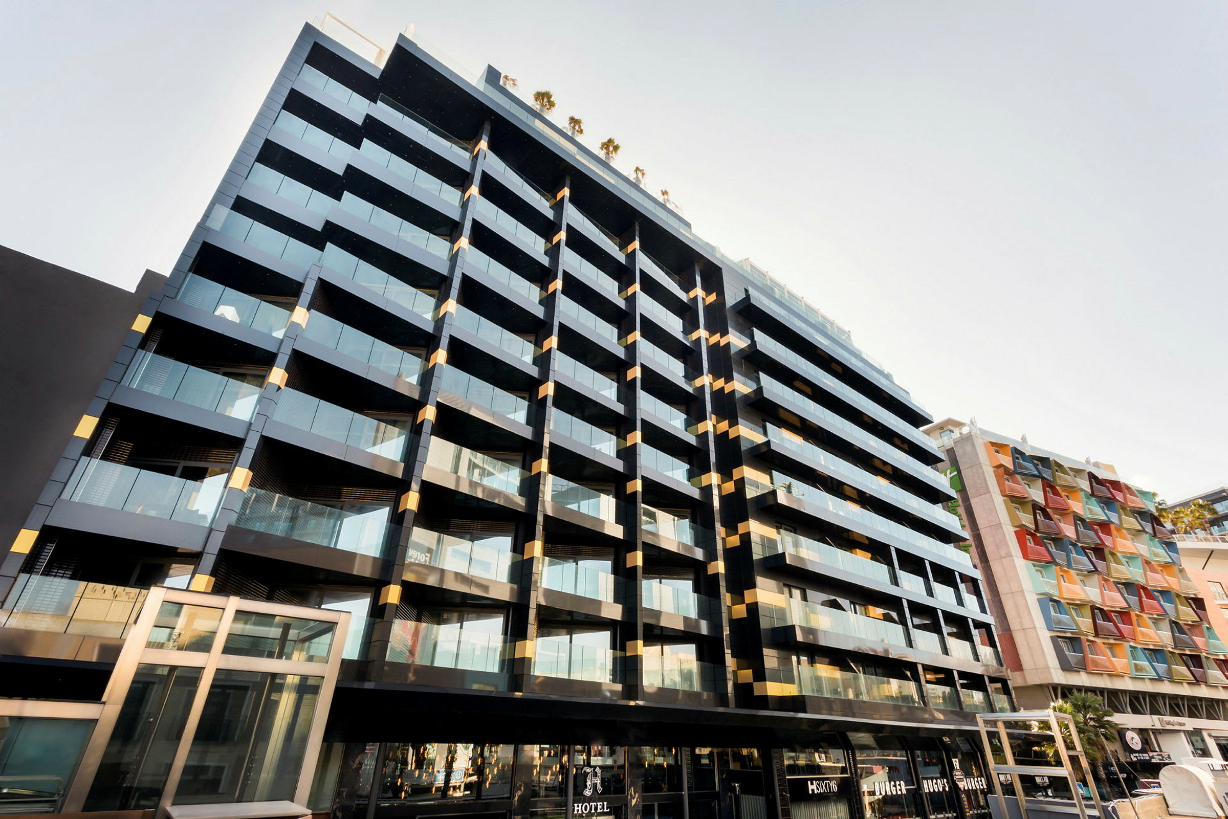 En moderne bygning med glassfasader og balkonger. Ved siden av en annen bygning med fargede paneler. (AI-generert tekst)