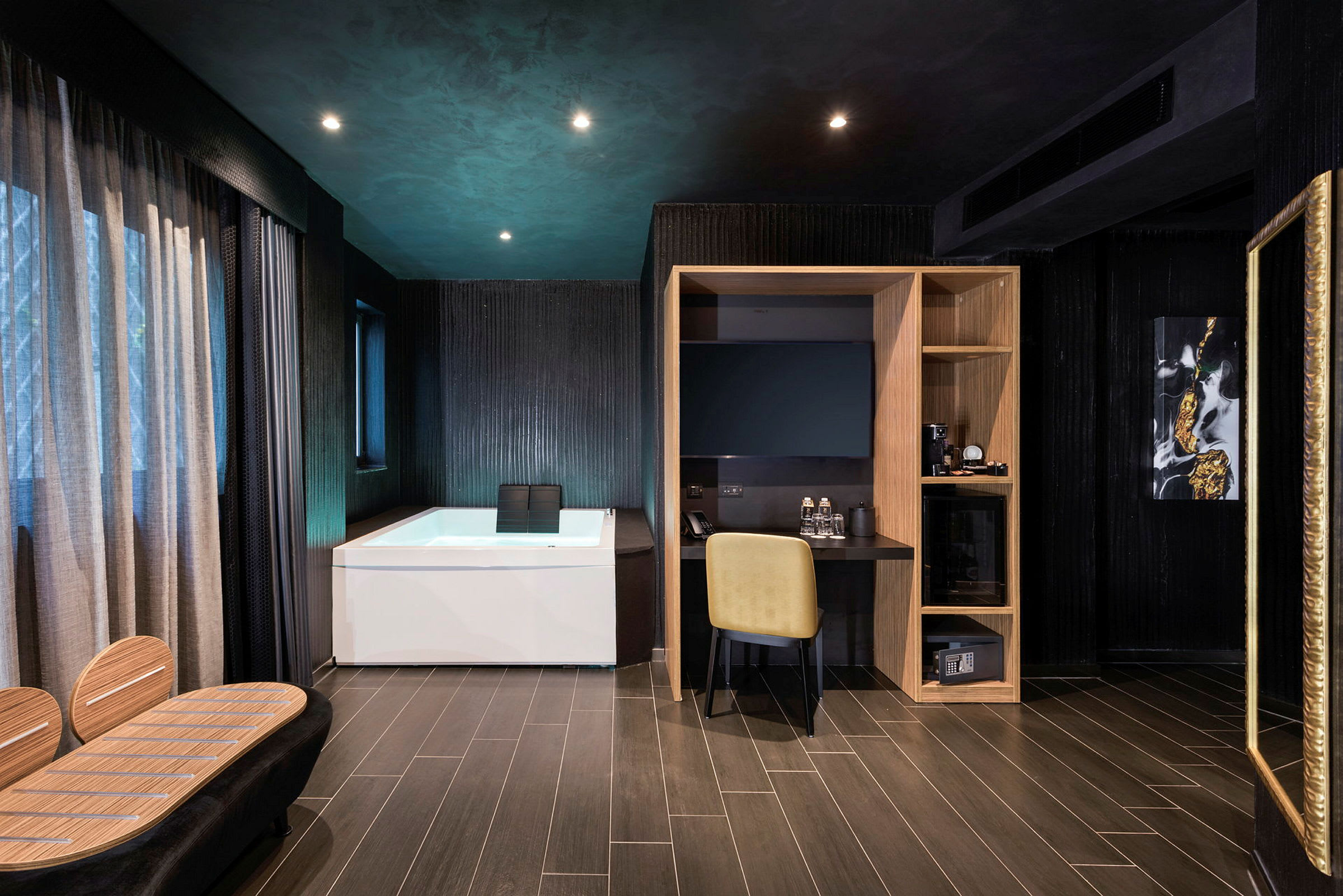 Et moderne hotellrom med mørke vegger, et hvitt badekar, et skrivebord med en gul stol og en trehylle. (AI-generert tekst)