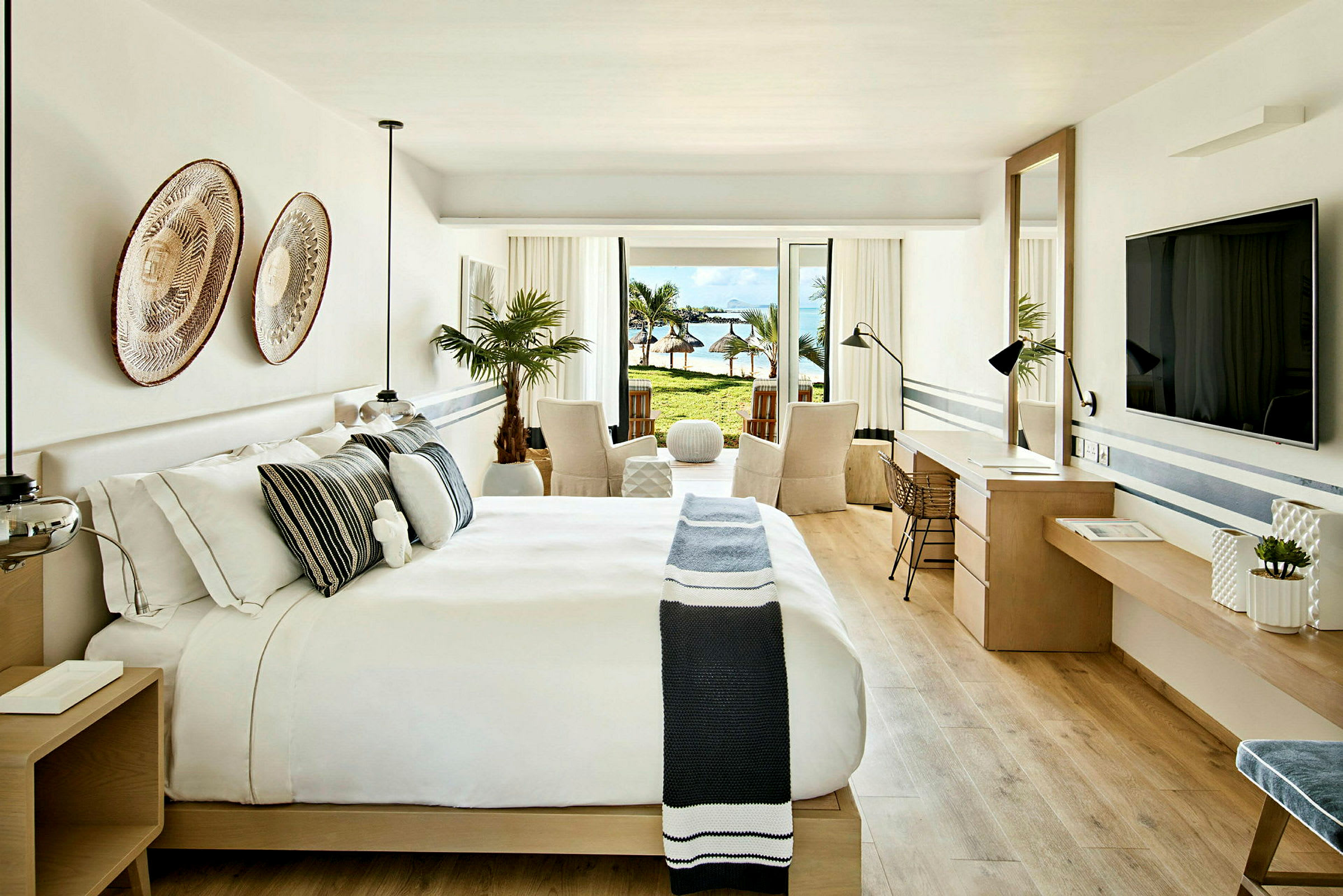 Et moderne hotellrom med dobbeltseng og innredning i lyse toner. Utgang til en balkong med utsikt over stranden. (AI-generert tekst)