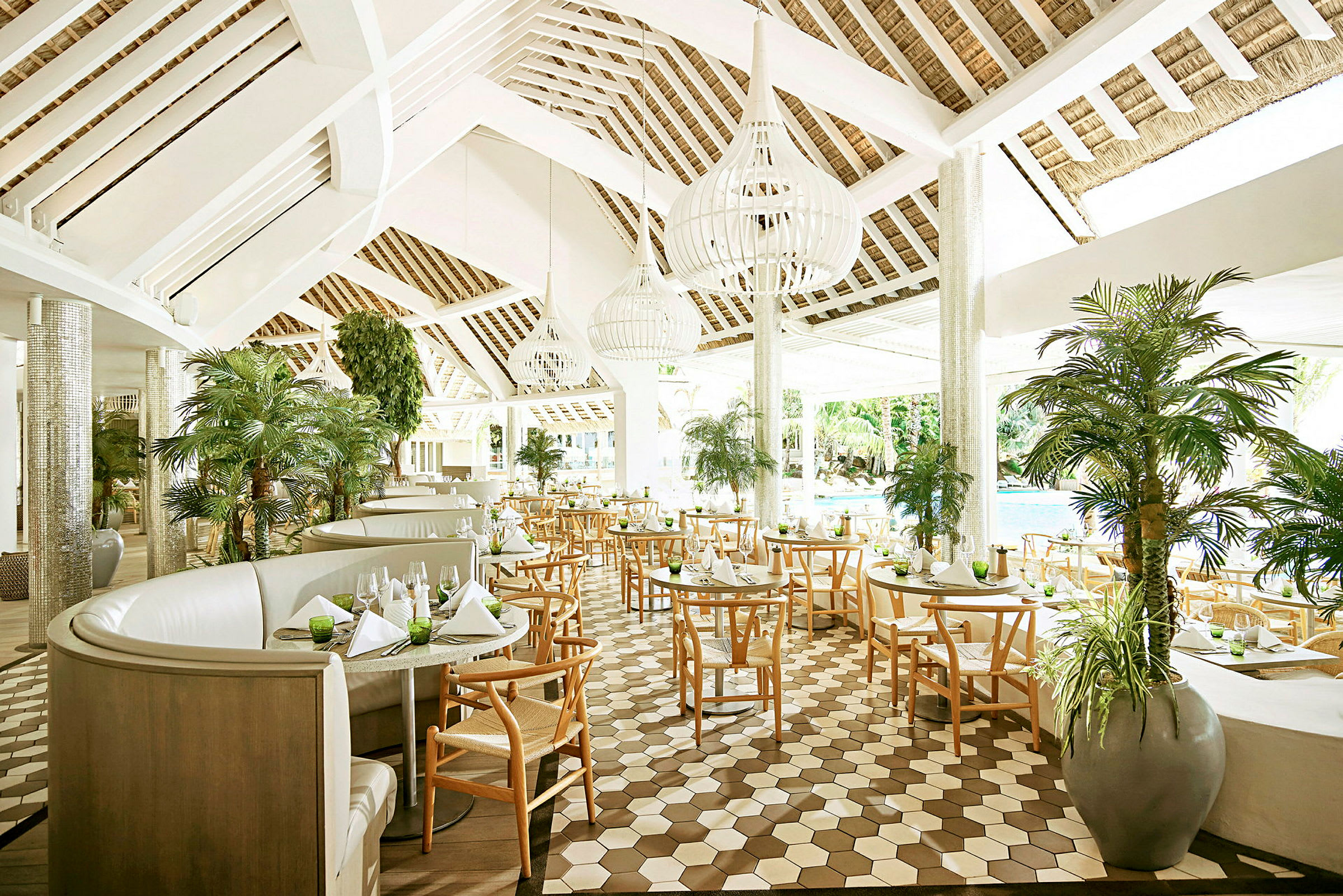 En restaurant med elegant interiør, lys takdesign, tremøbler og store glassvinduer mot et grønt utendørsområde. (AI-generert tekst)
