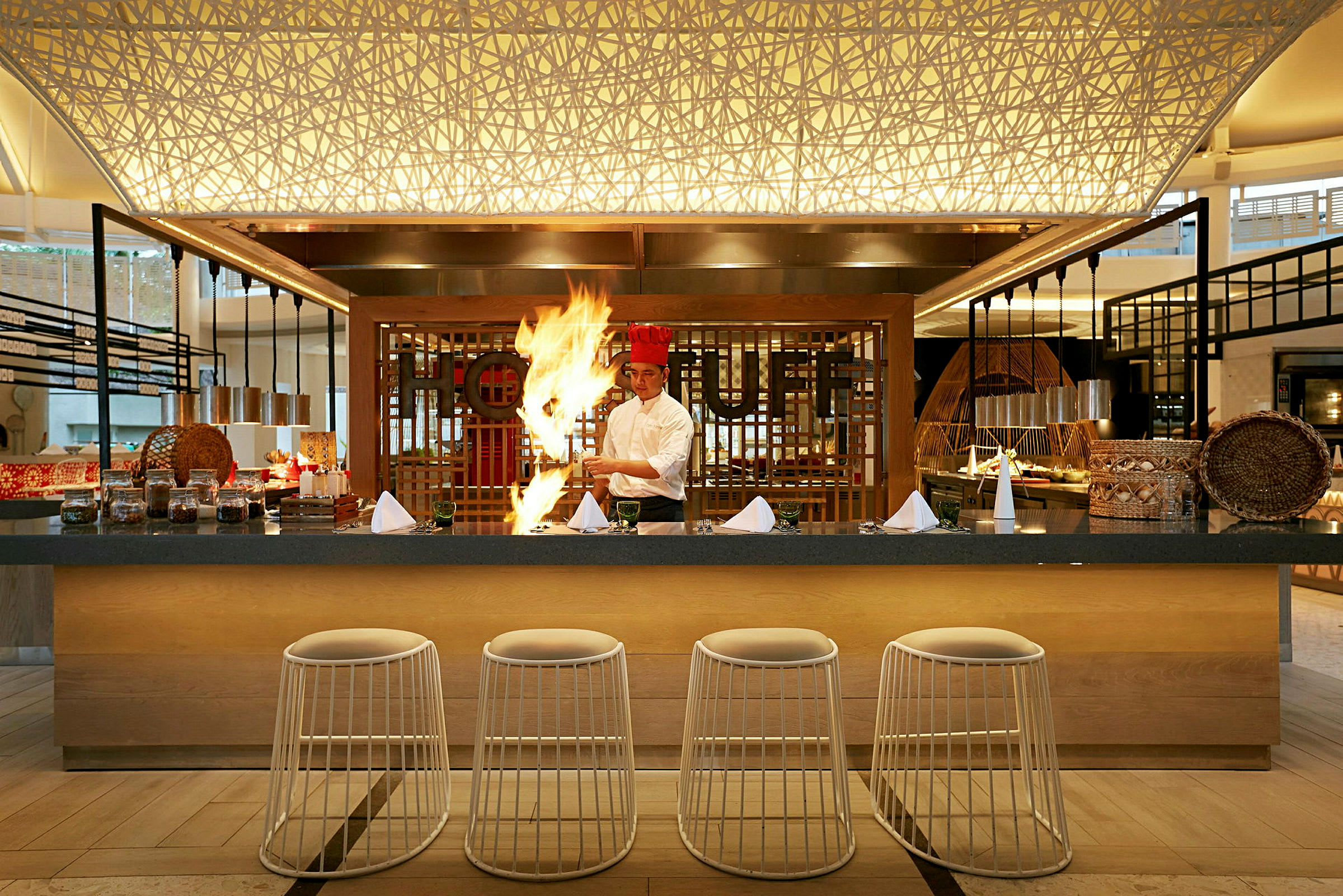 En kokk står ved en elegant restaurantdisk med flammer og matlaging. (AI-generert tekst)