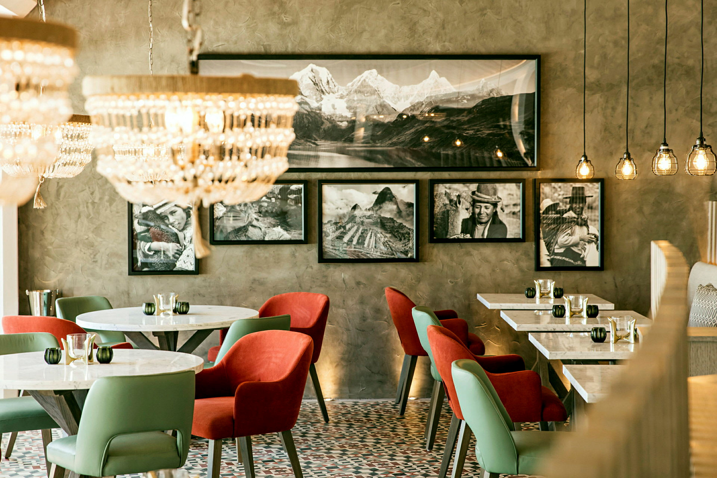 En moderne innredet kafé med marmorbord og fargerike stoler, dekorert med fotografier på veggen og elegante lysekroner i taket. (AI-generert tekst)