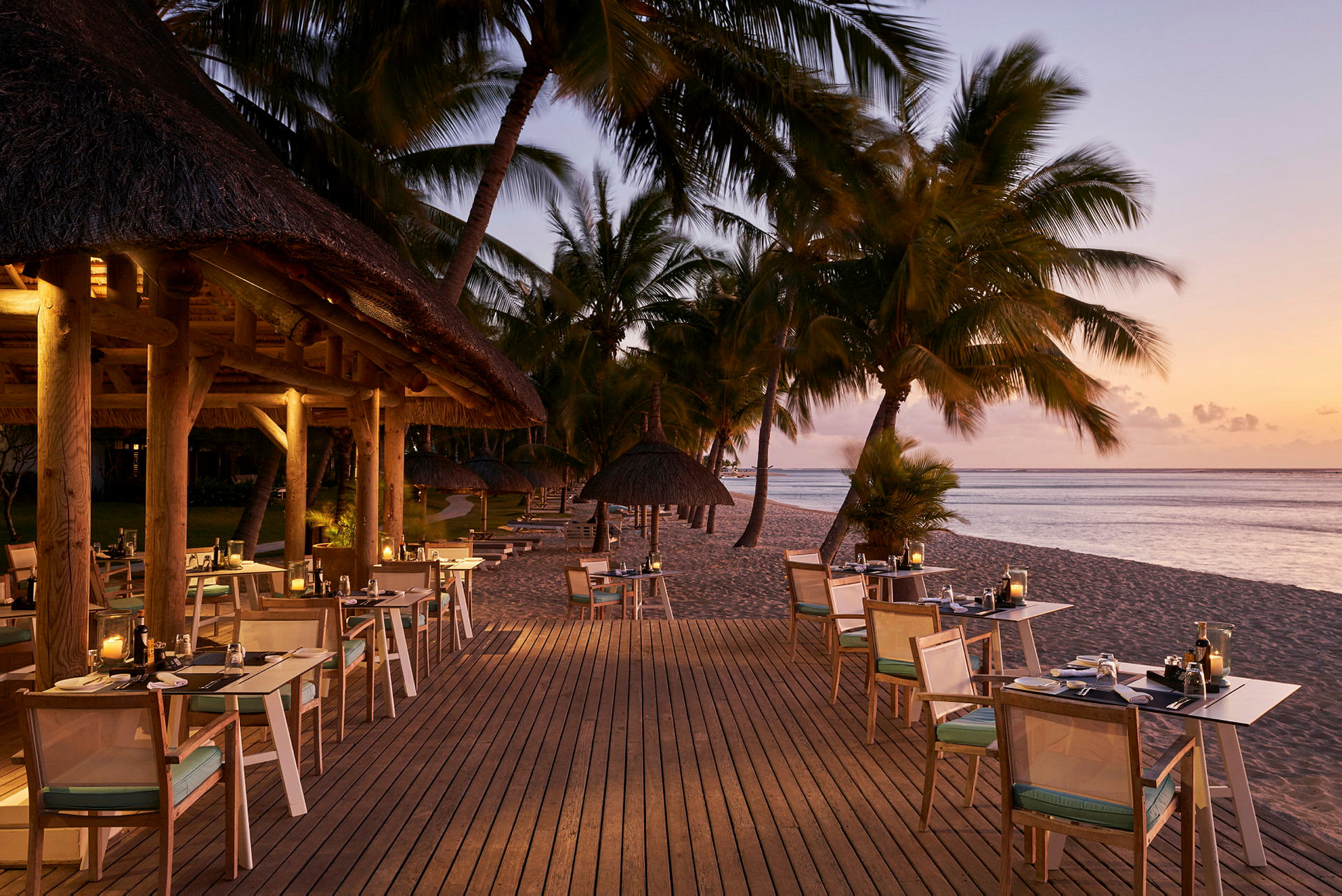 Utendørs servering på en tret terrasse ved havet med solnedgang og palmer. (AI-generert tekst)