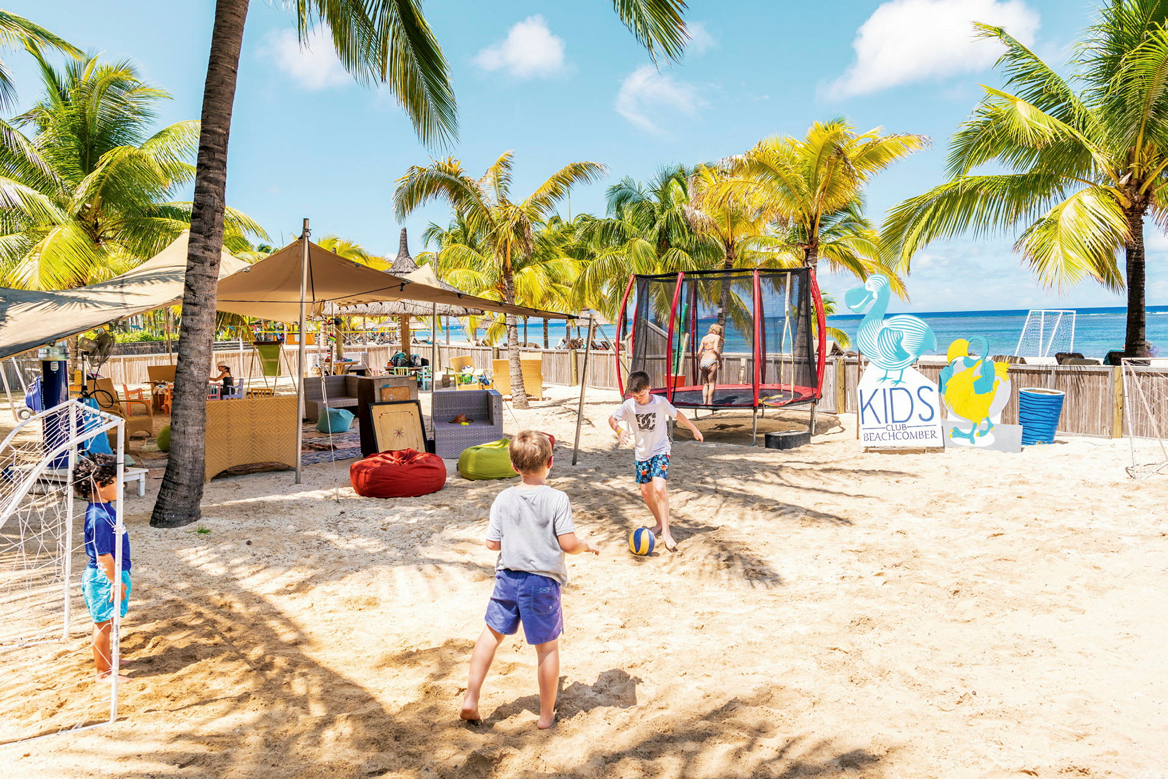 Barn leker på en sandstrand ved siden av en trampoline og skilt for Kids Club. (AI-generert tekst)