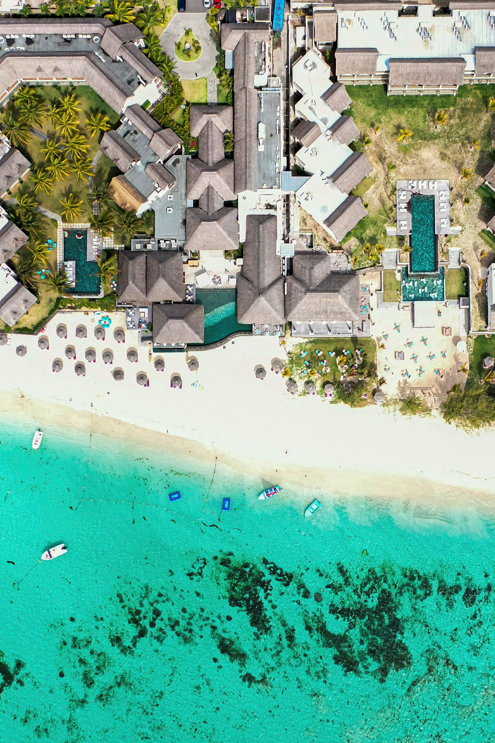 Flyfoto av et hotellkompleks ved en strand med turkis vann. (AI-generert tekst)