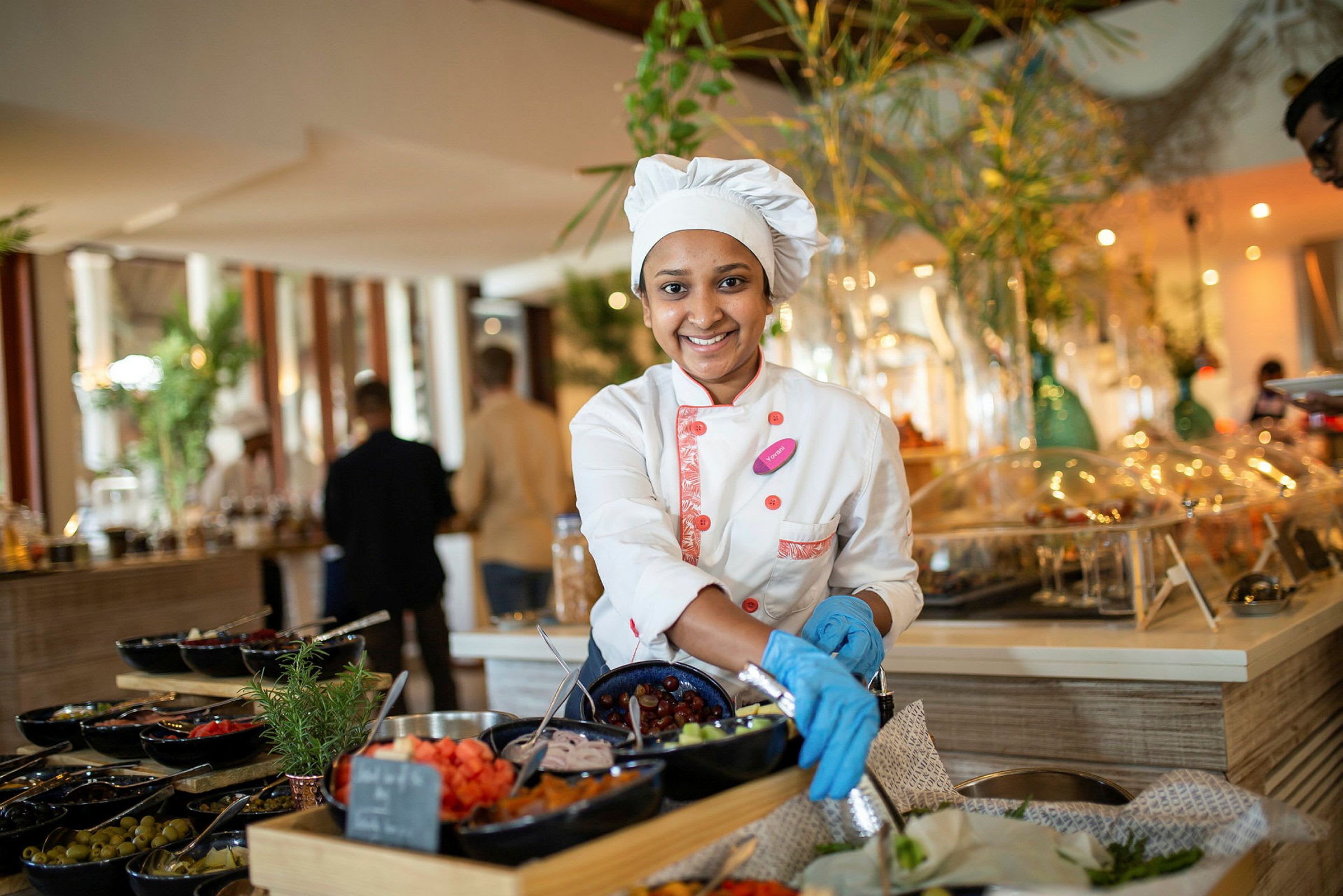 En person i arbeidsklær ordner mat på en buffet fylt med forskjellige retter. (AI-generert tekst)