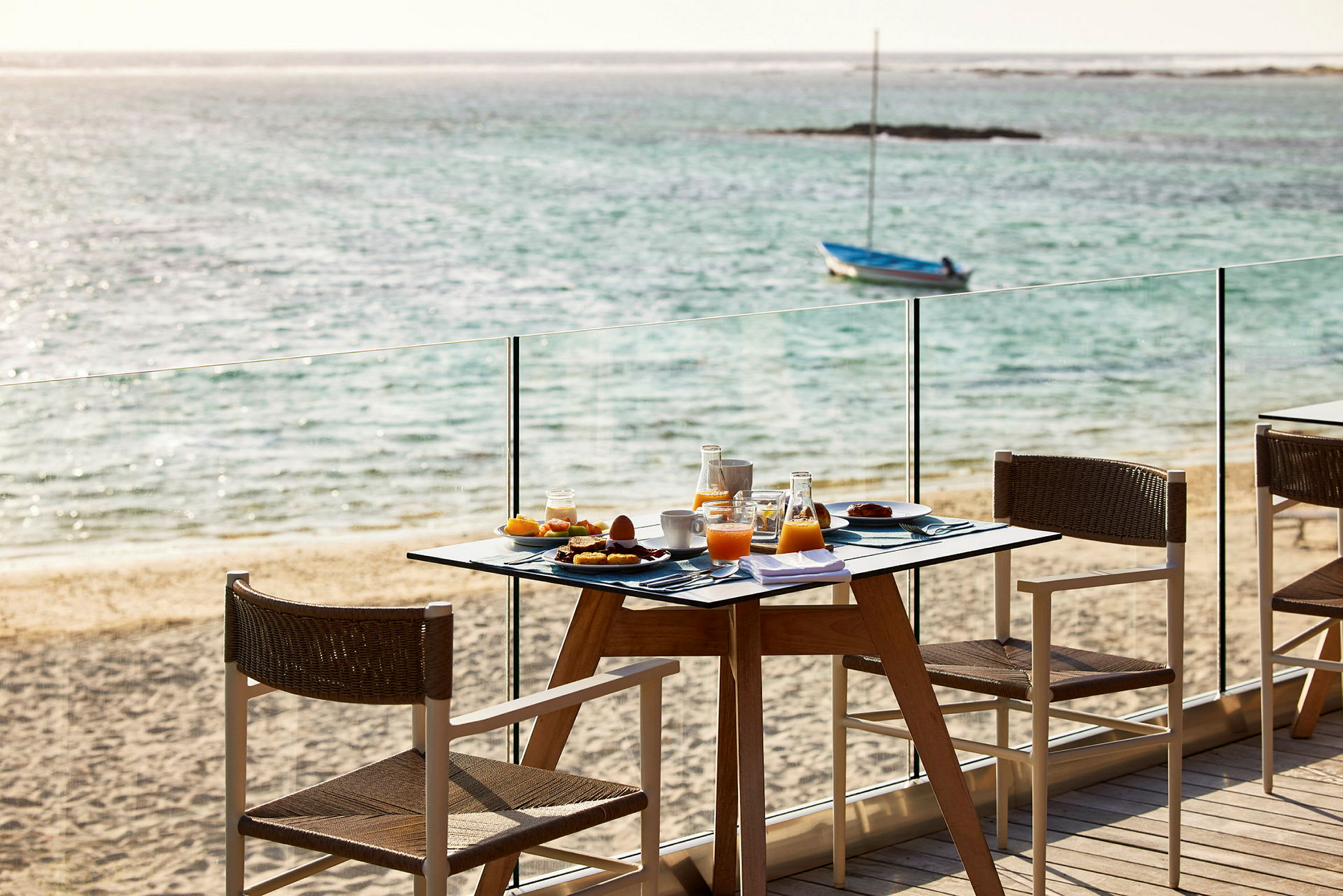 En frokost serveres ved et bord nær stranden med havet i bakgrunnen. (AI-generert tekst)