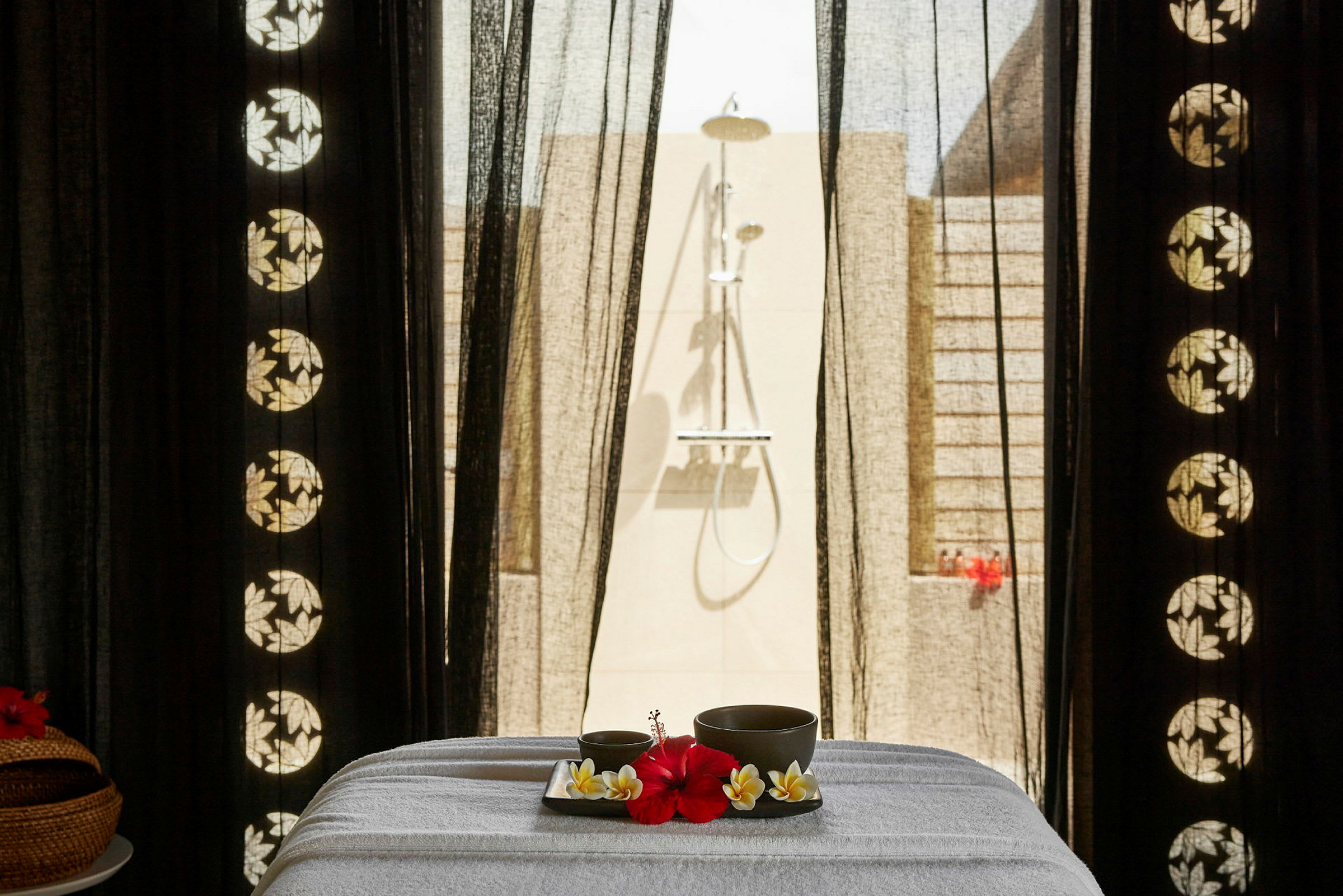 Et spa-bord med et brett som inneholder en rød blomst og drikkebeger, plassert foran en utendørs dusj. (AI-generert tekst)