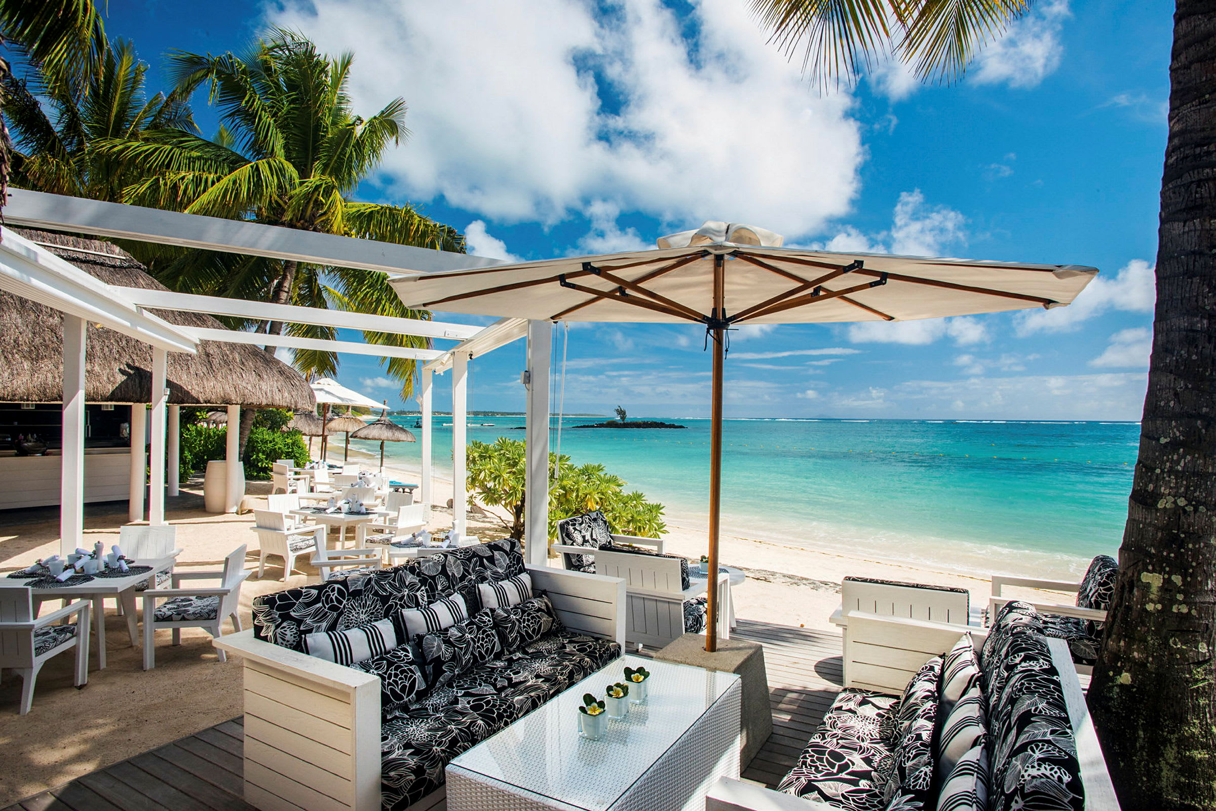 Restaurantområde ved stranden med sitteplasser, parasoller og utsikt over havet. (AI-generert tekst)