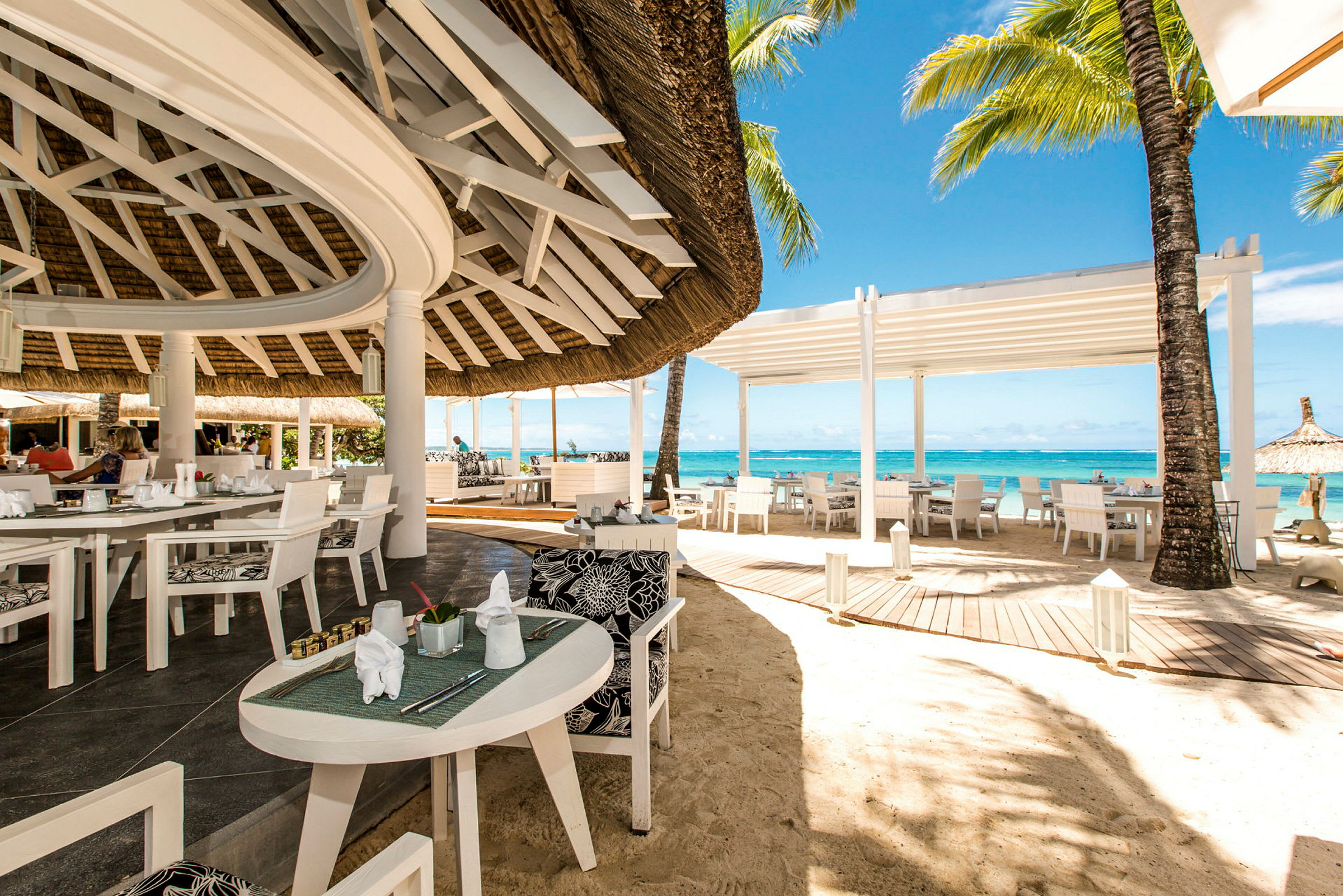 En åpen restaurant ved stranden med hvite møbler og utsikt over havet. (AI-generert tekst)