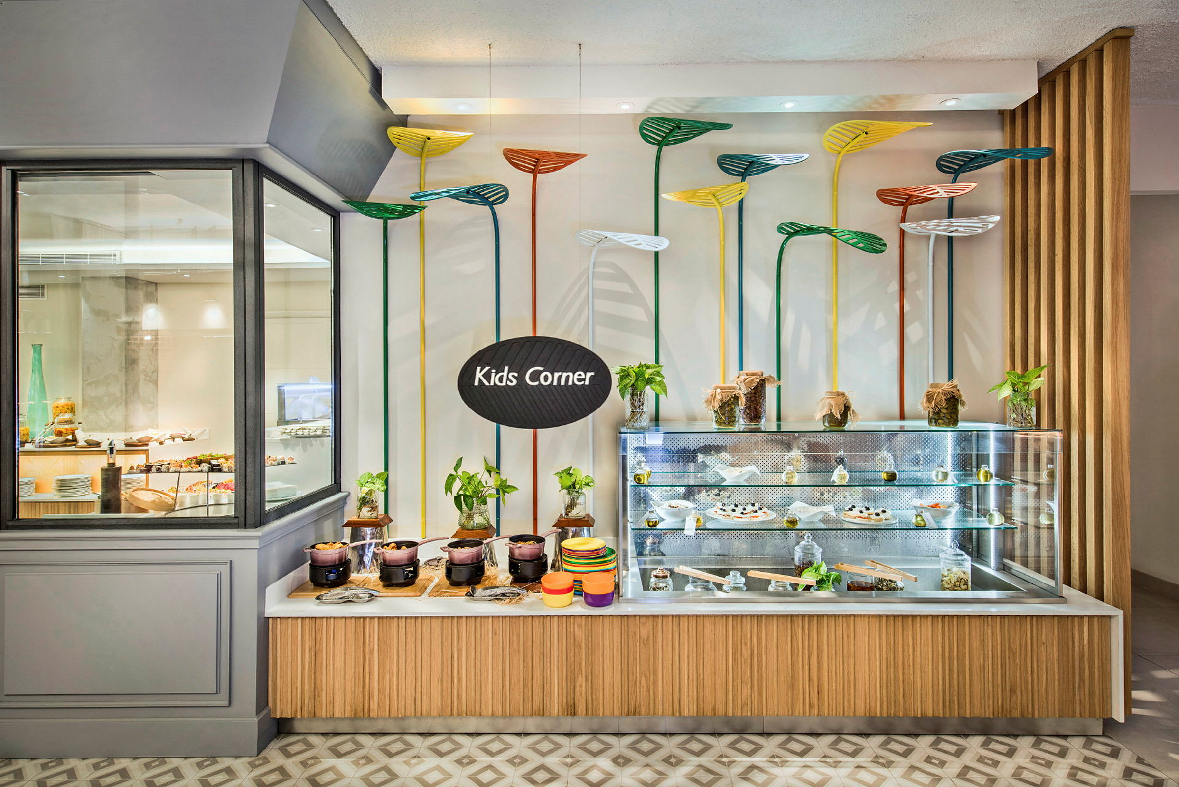 Et matområde for barn merket med skiltet "Kids Corner" med en utstillingsdisk fylt med måltider og dekorert med fargerike, planteaktige designelementer. (AI-generert tekst)