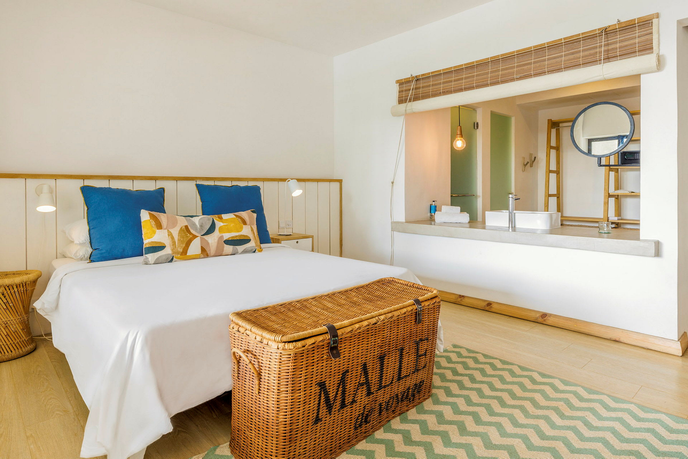 Et lyst hotellrom med en dobbeltseng og en kurv ved fotenden. (AI-generert tekst)