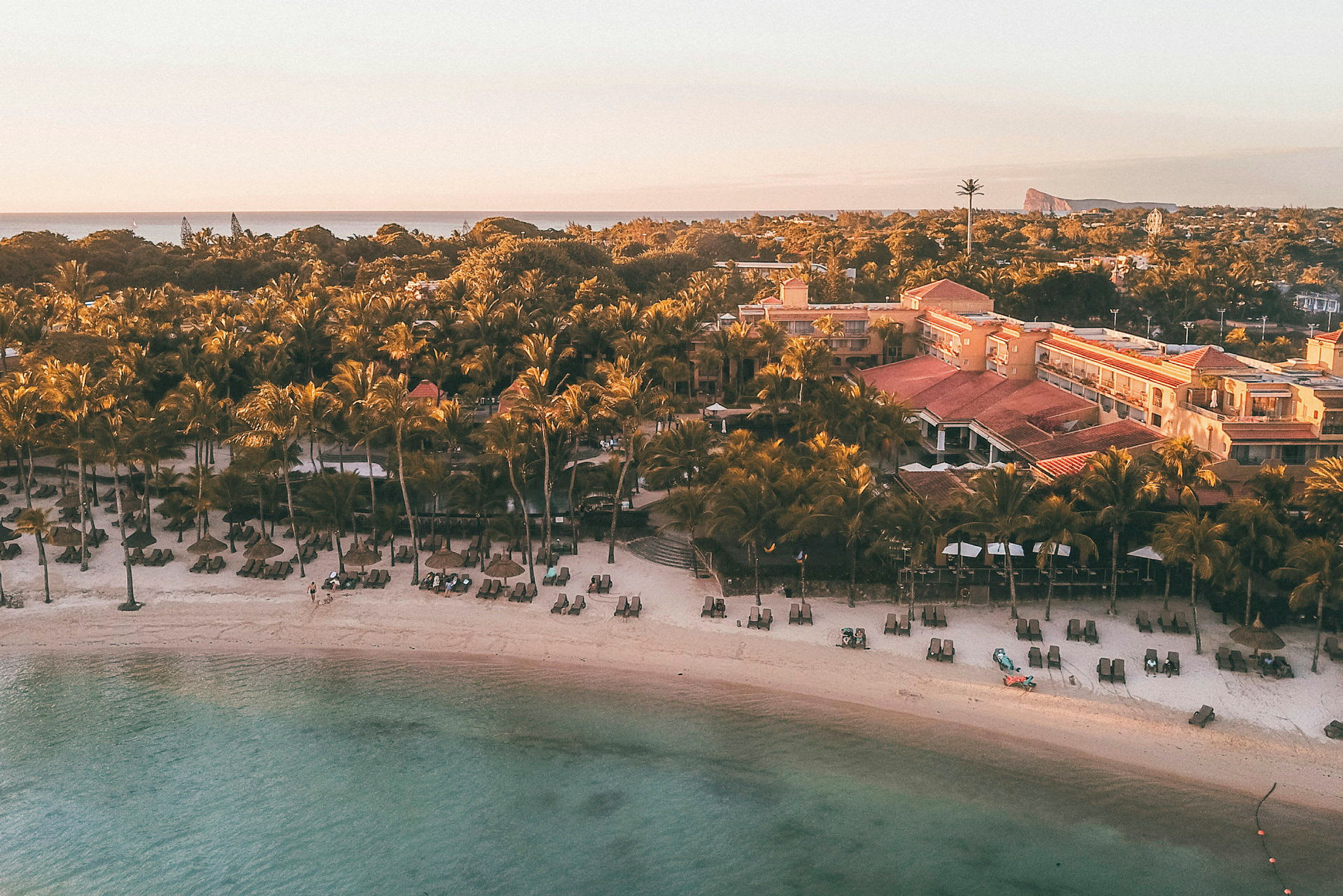 Strand med solsenger og parasoller foran en resort og palmer ved havet. (AI-generert tekst)