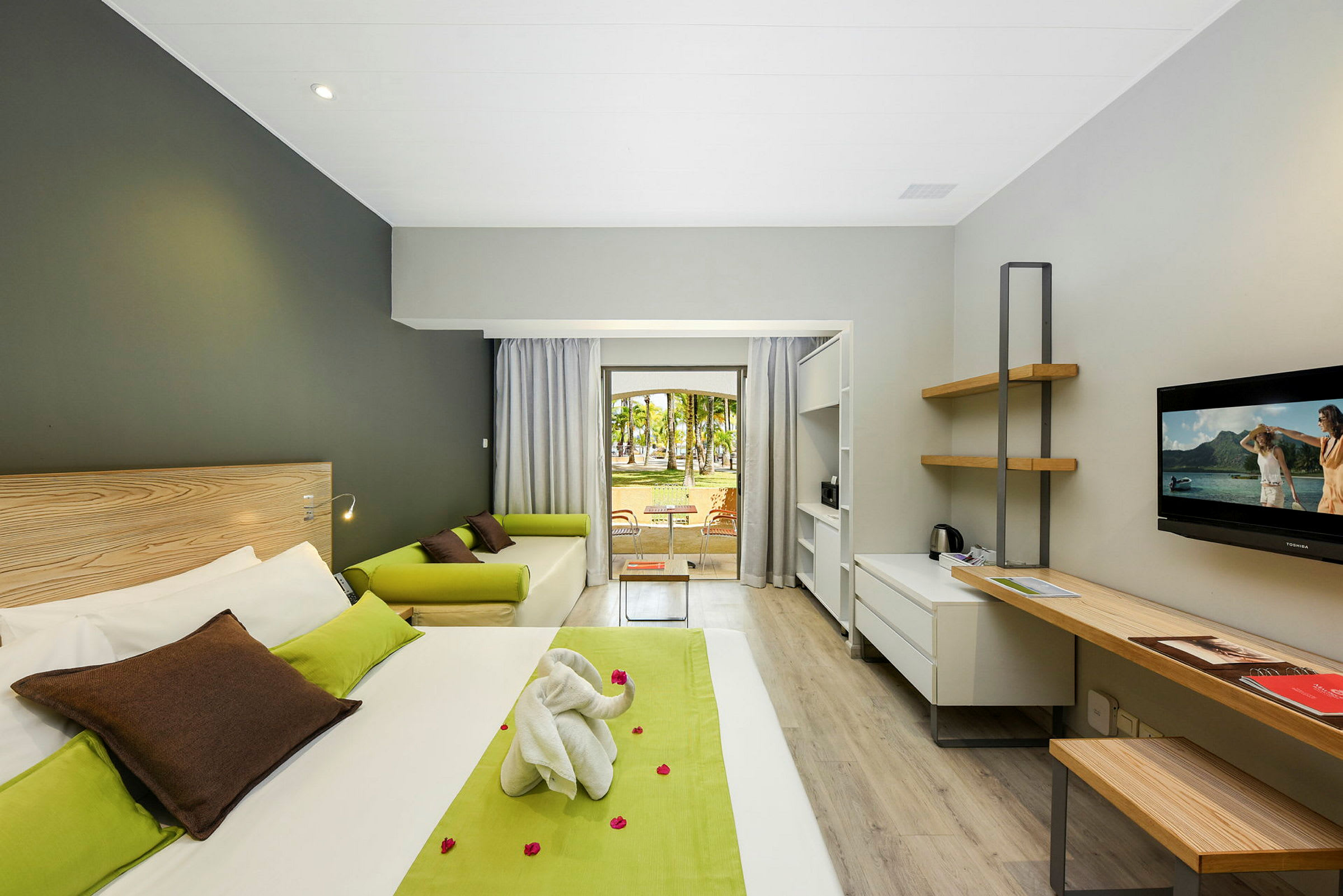 Moderne hotellrom med seng, skrivebord, sofa og utsikt mot en hage. (AI-generert tekst)