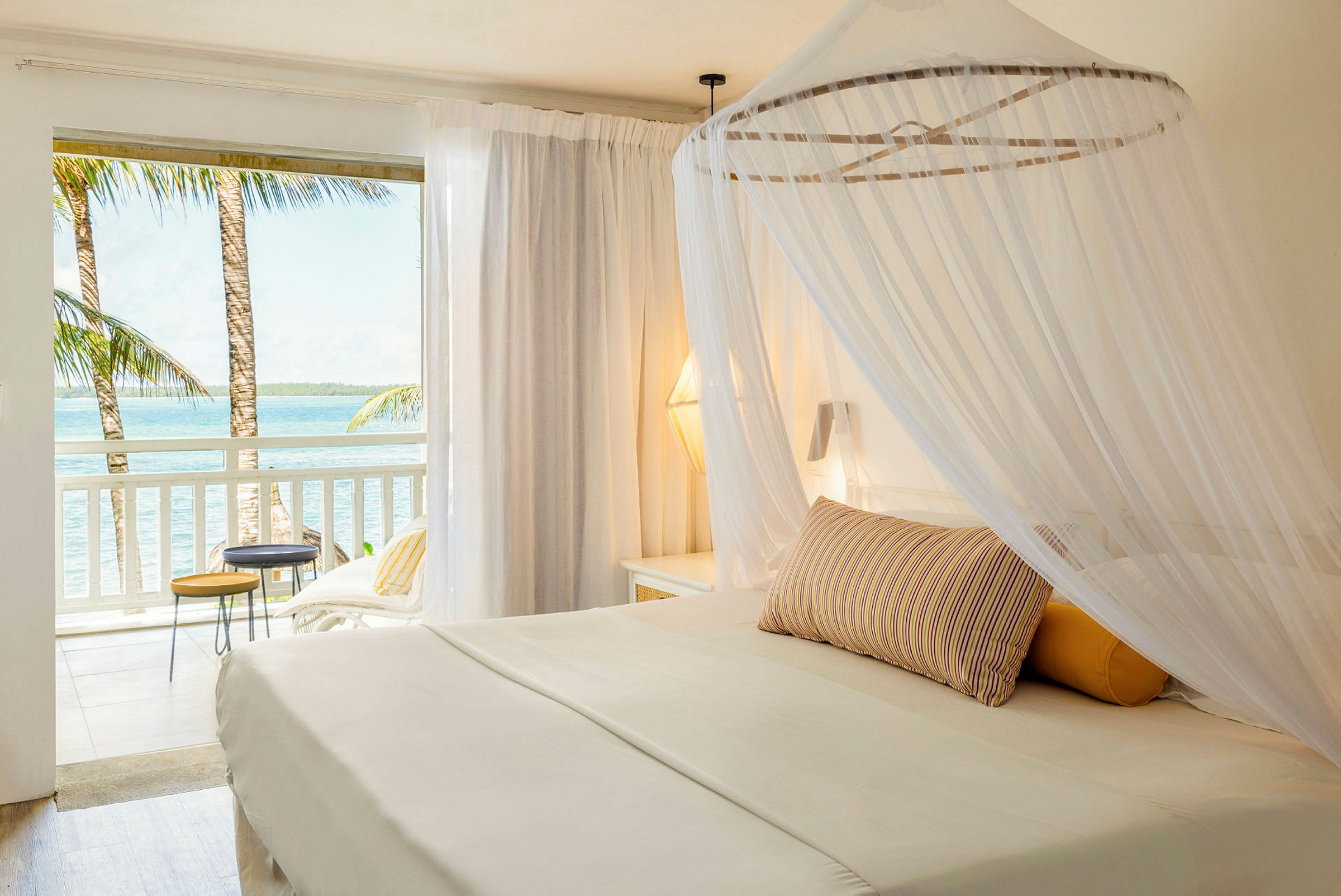 En lys hotellsuite med himmelseng og utsikt over havet fra balkongen. (AI-generert tekst)