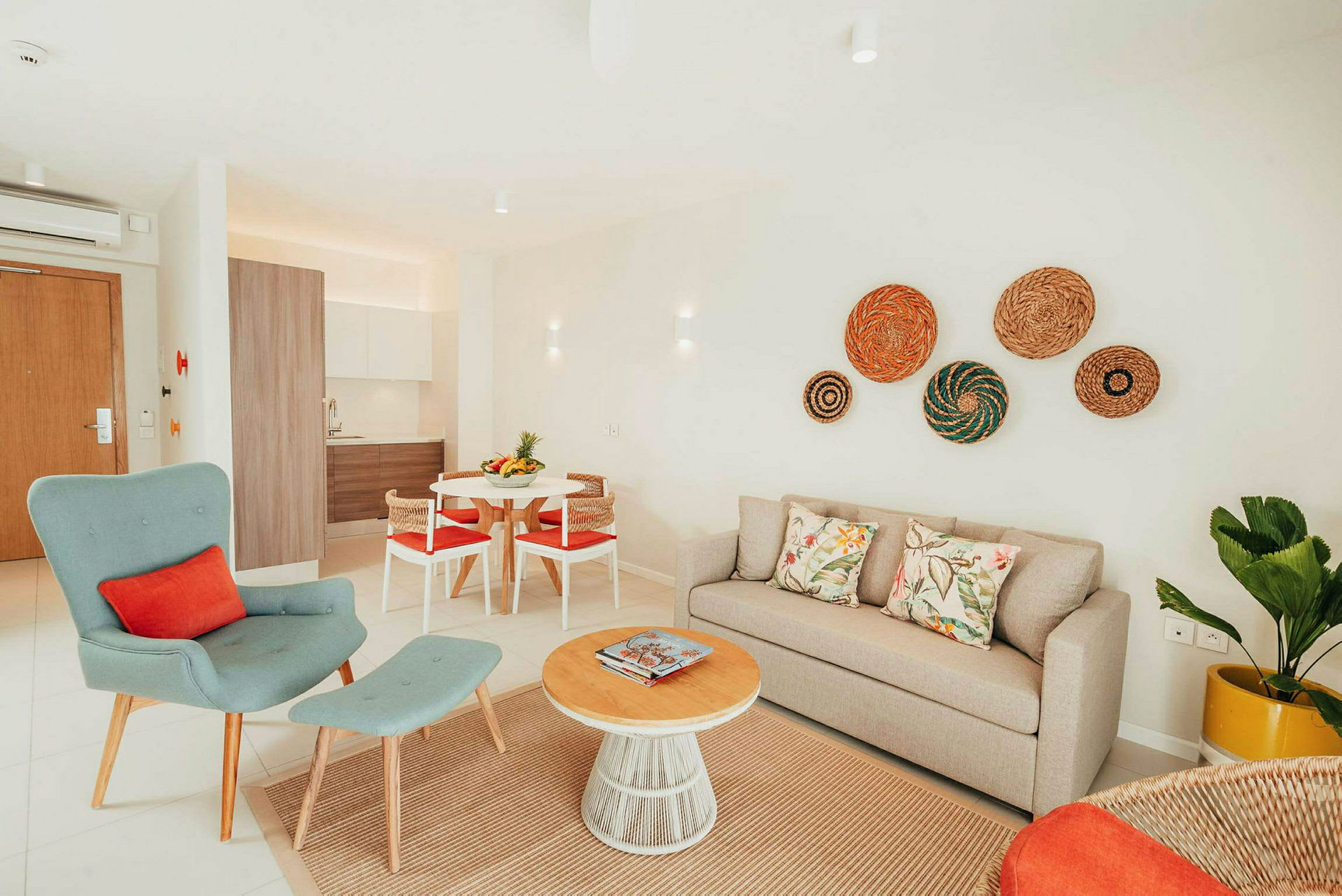 En lys og moderne innredet stue med beige sofa, grønn lenestol og et rundt salongbord av tre. Kjøkkenet er synlig i bakgrunnen. (AI-generert tekst)