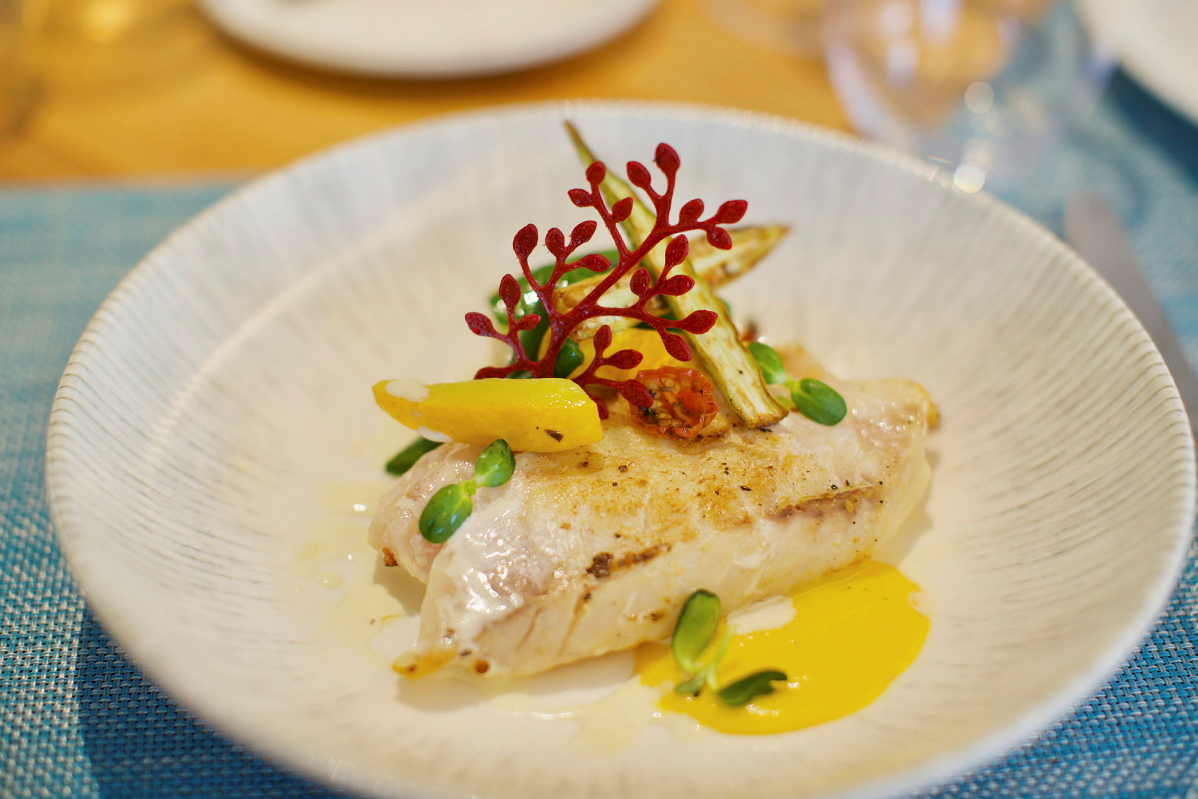 En tallerken med en elegant anrett rett bestående av grillet fiskefilet med grønnsaker og saus. (AI-generert tekst)