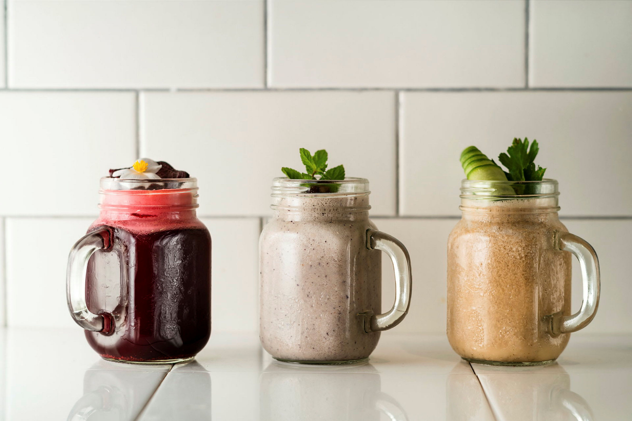 Tre forskjellige smoothies i glasskrukker på en hvit overflate. (AI-generert tekst)