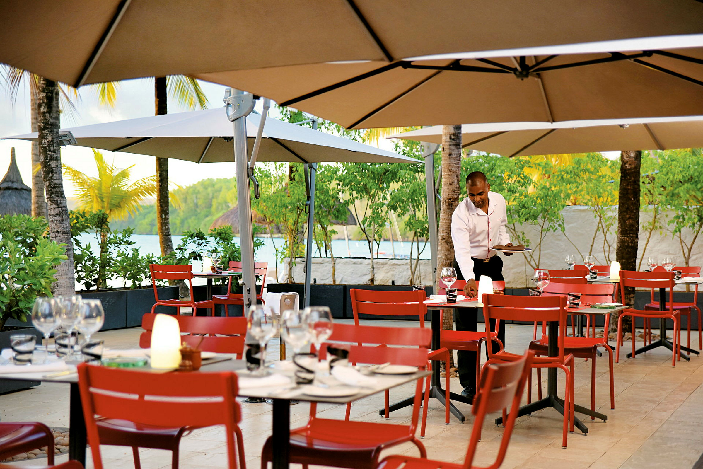 Restaurant med uteservering, røde stoler og bord under parasoller. (AI-generert tekst)