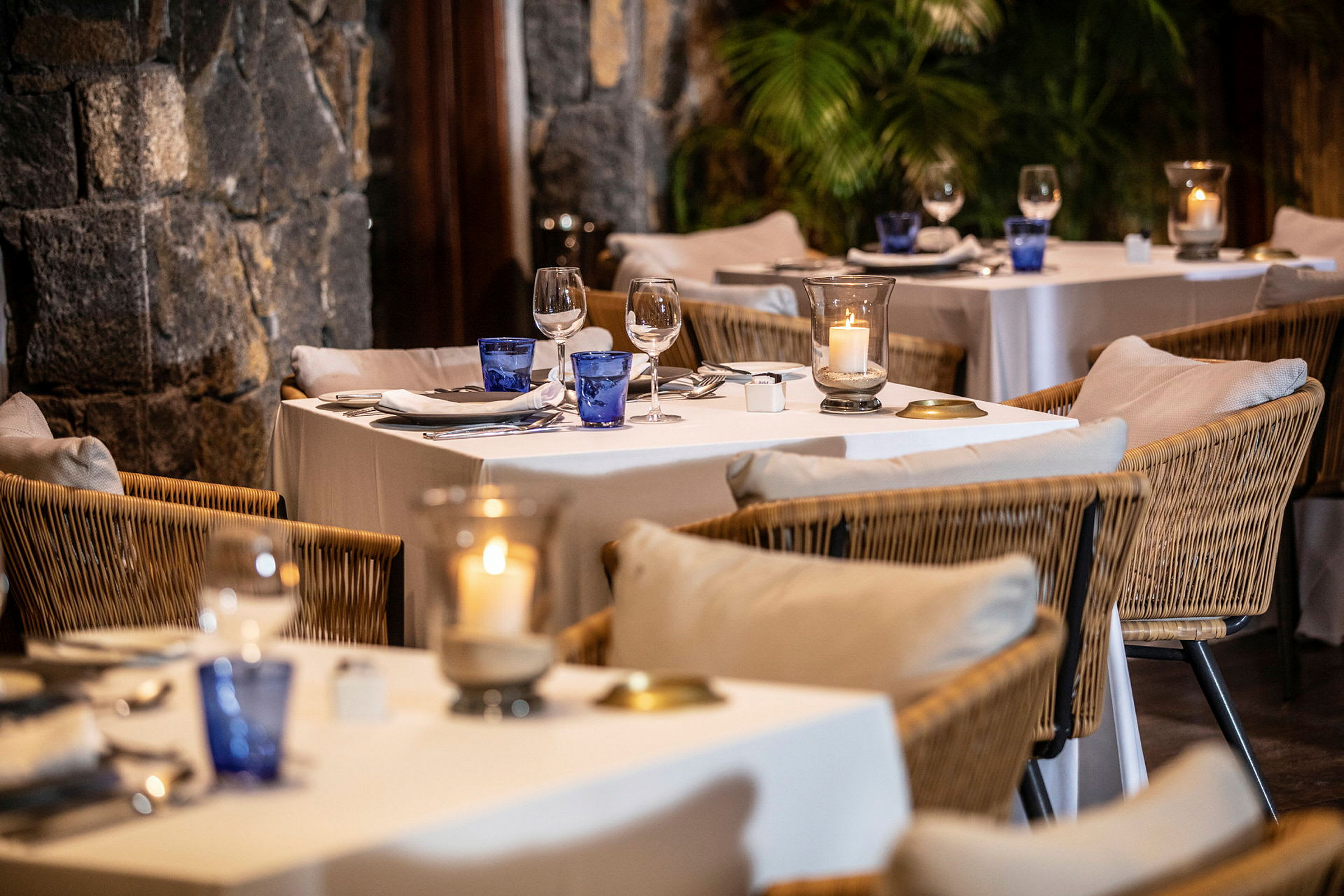 Et elegant dekket bord i en restaurant med rottingstoler og hvite linduker. (AI-generert tekst)