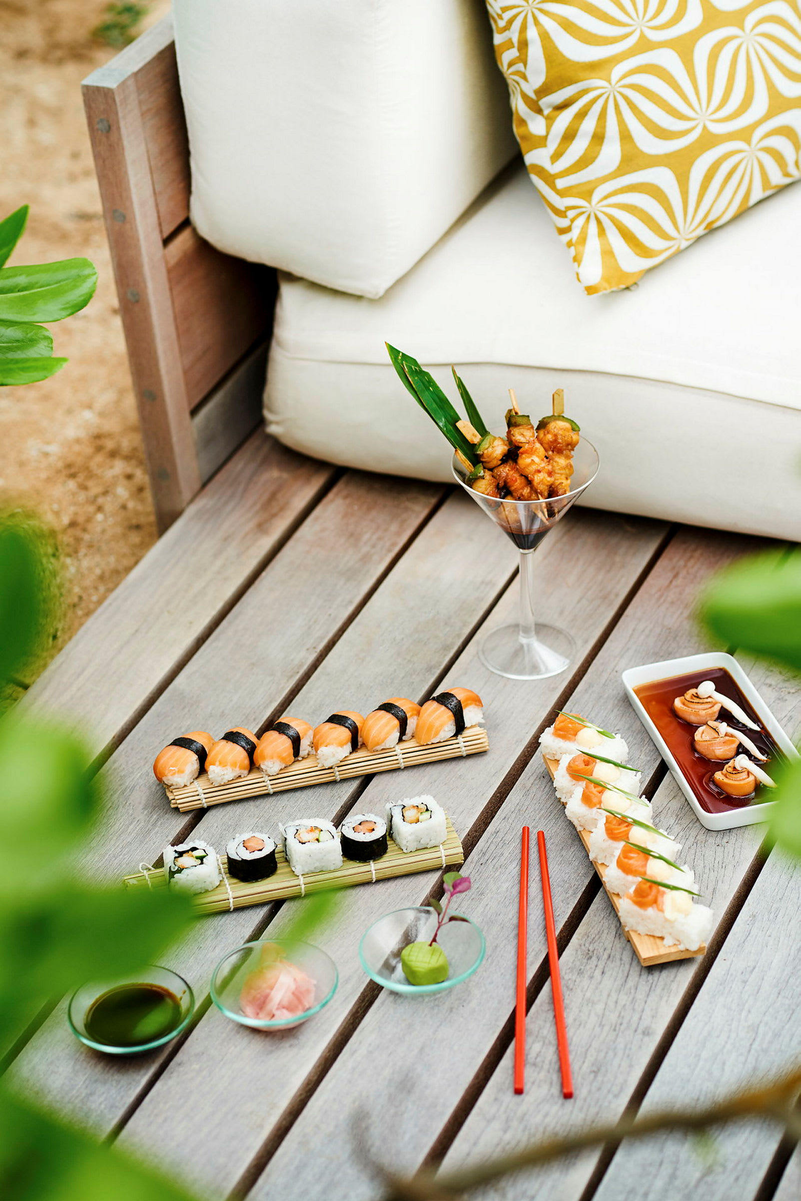 Et bord med sushi, grillspyd og tilbehør ved siden av en hvit sofa. (AI-generert tekst)