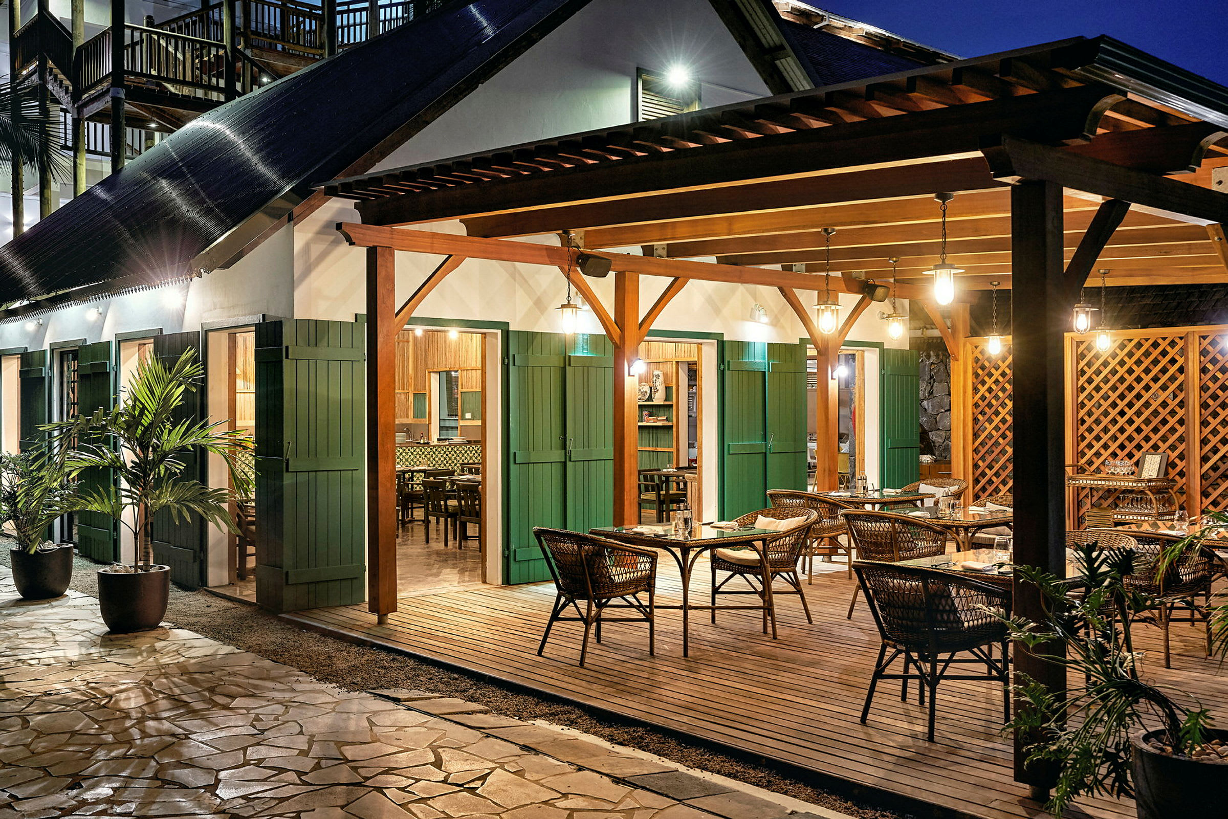 En utendørsrestaurant med bord og stoler under en trepaviljong med belysning. (AI-generert tekst)
