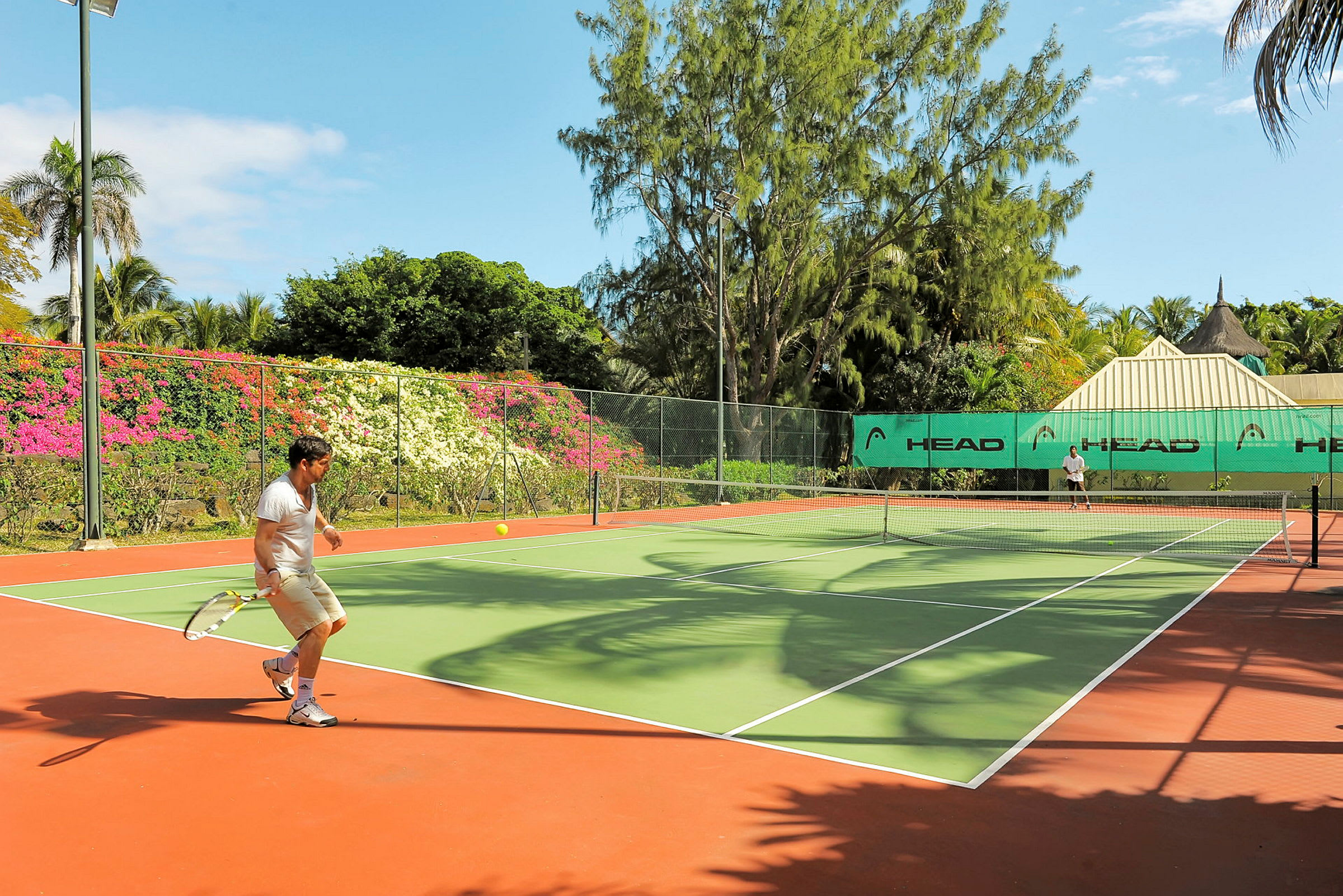 En tennisbane omgitt av grøntområder og fargerike blomster. (AI-generert tekst)