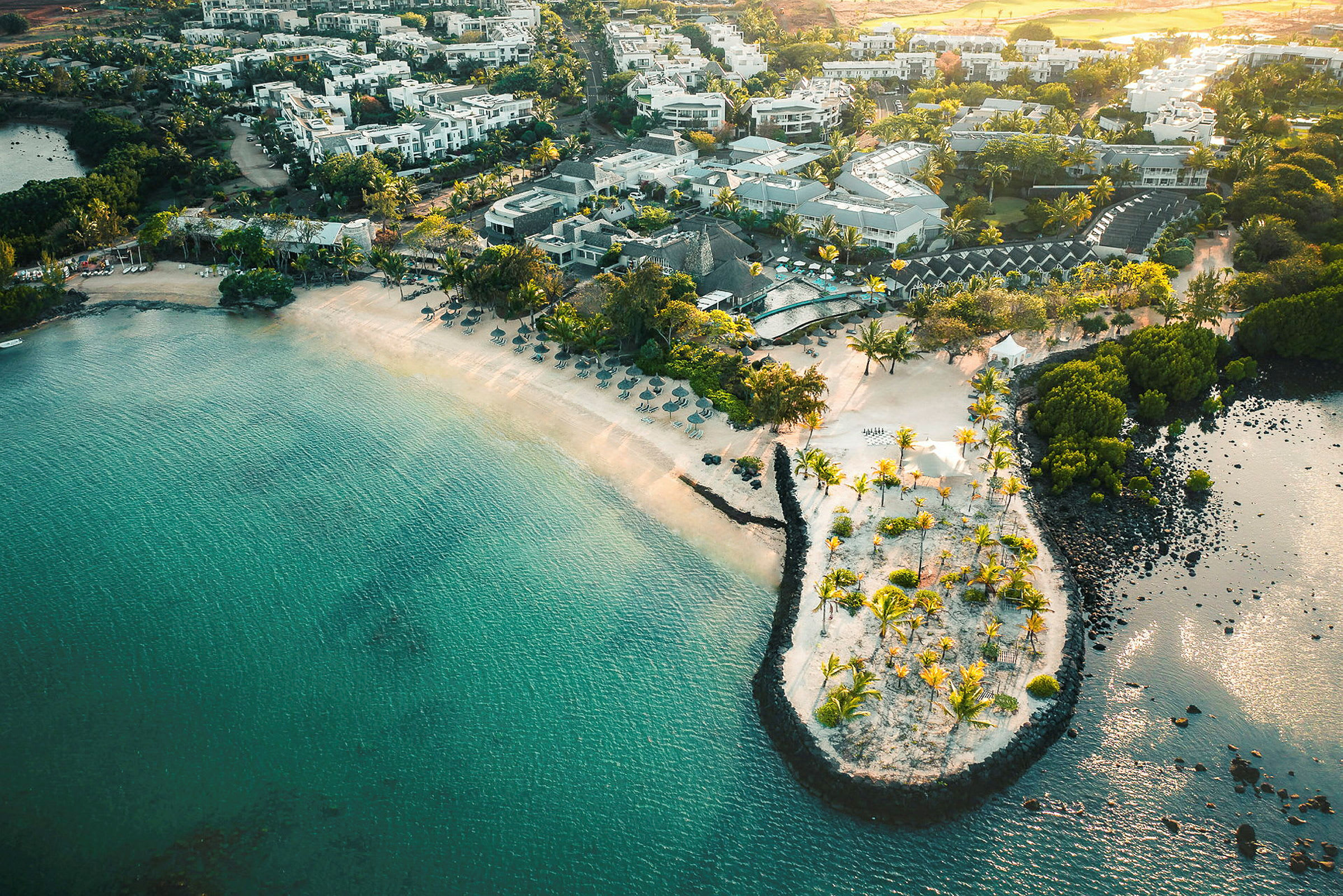 Flyfoto av en kystresort med sandstrand, turkis vann og palmer. (AI-generert tekst)
