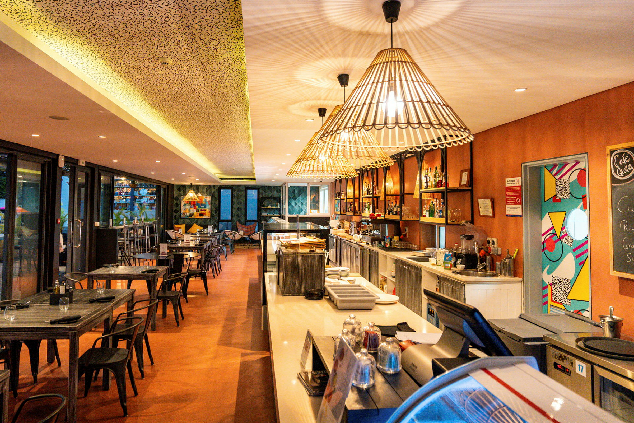 Interiør av en restaurant med bord og stoler, en bardisk og dekorative lamper. (AI-generert tekst)