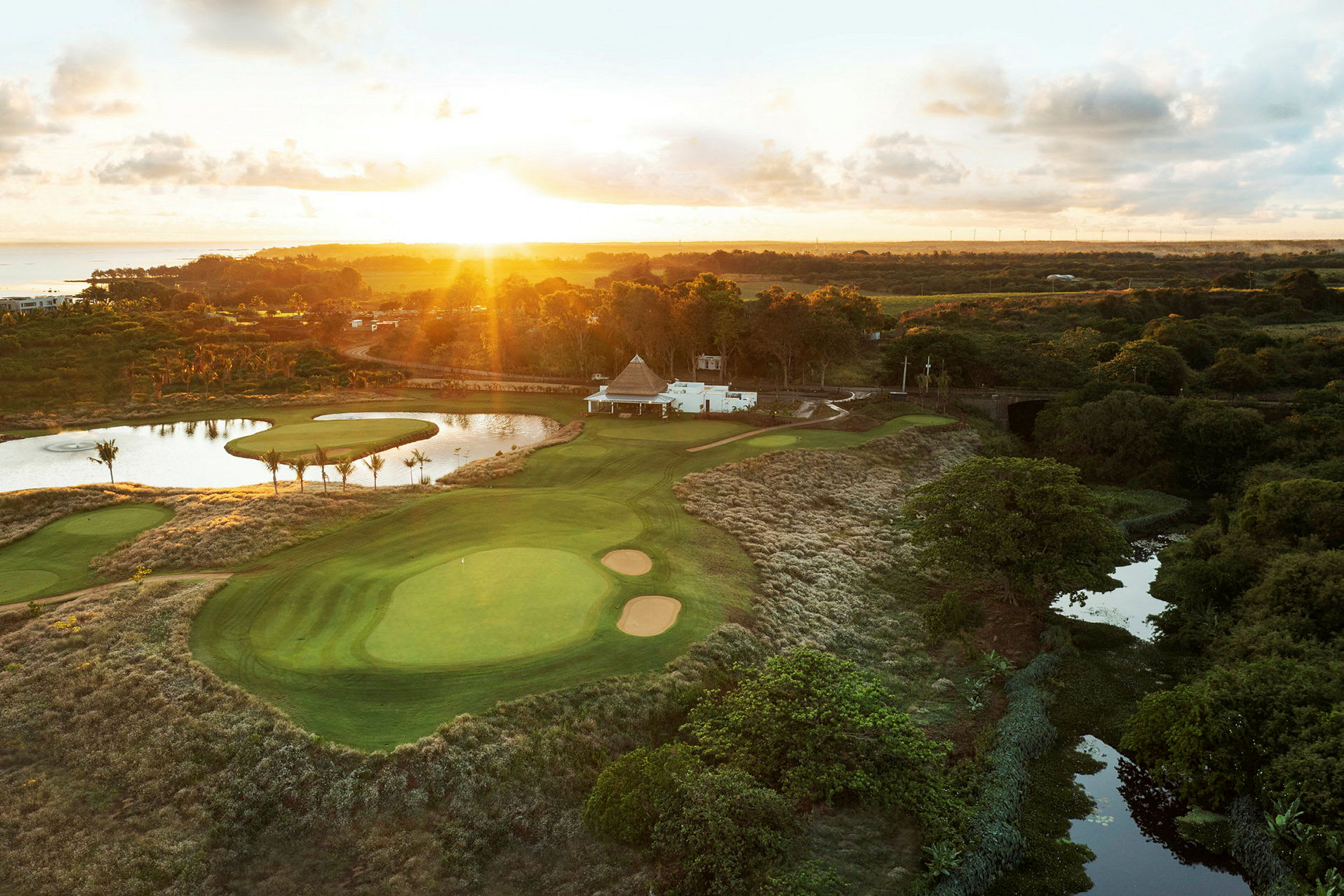 En golfbane med grønne fairways, bunkere og en dam, omgitt av vegetasjon under solnedgang. (AI-generert tekst)
