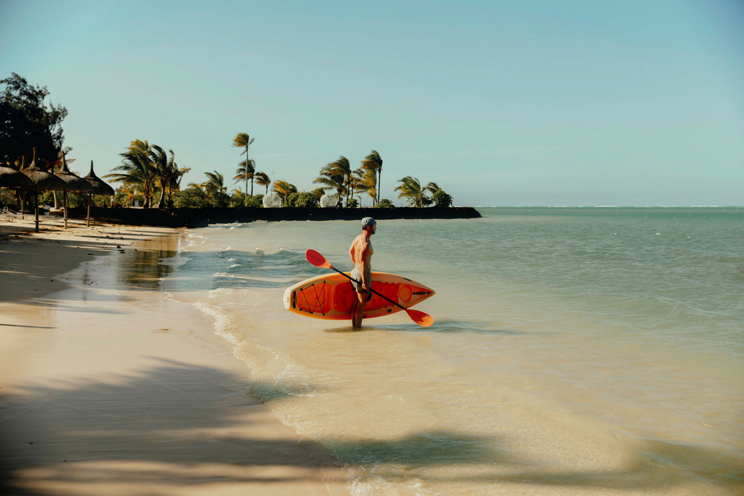 En person står på en sandstrand med et paddleboard og en padle ved vannet. (AI-generert tekst)