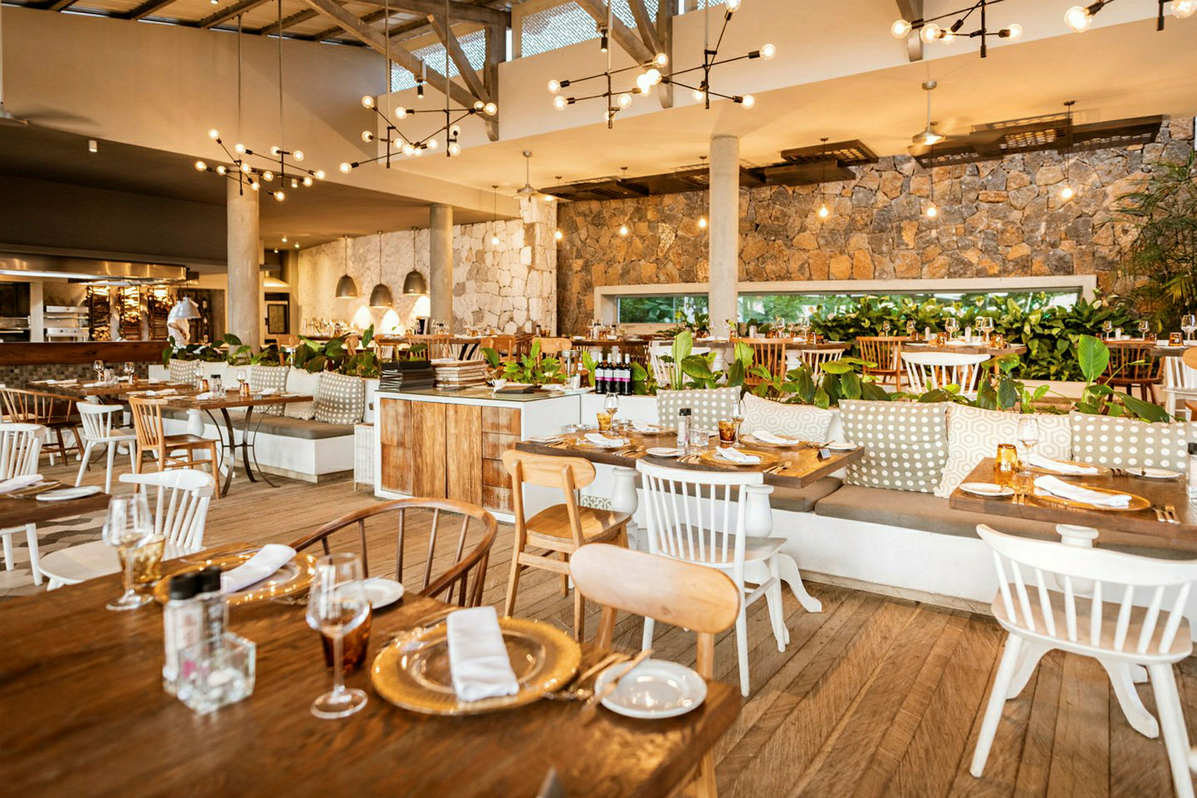 Innendørs interiør av en restaurant med trebord og stoler, murvegger, hengende lamper og grønne planter som dekorasjon. (AI-generert tekst)